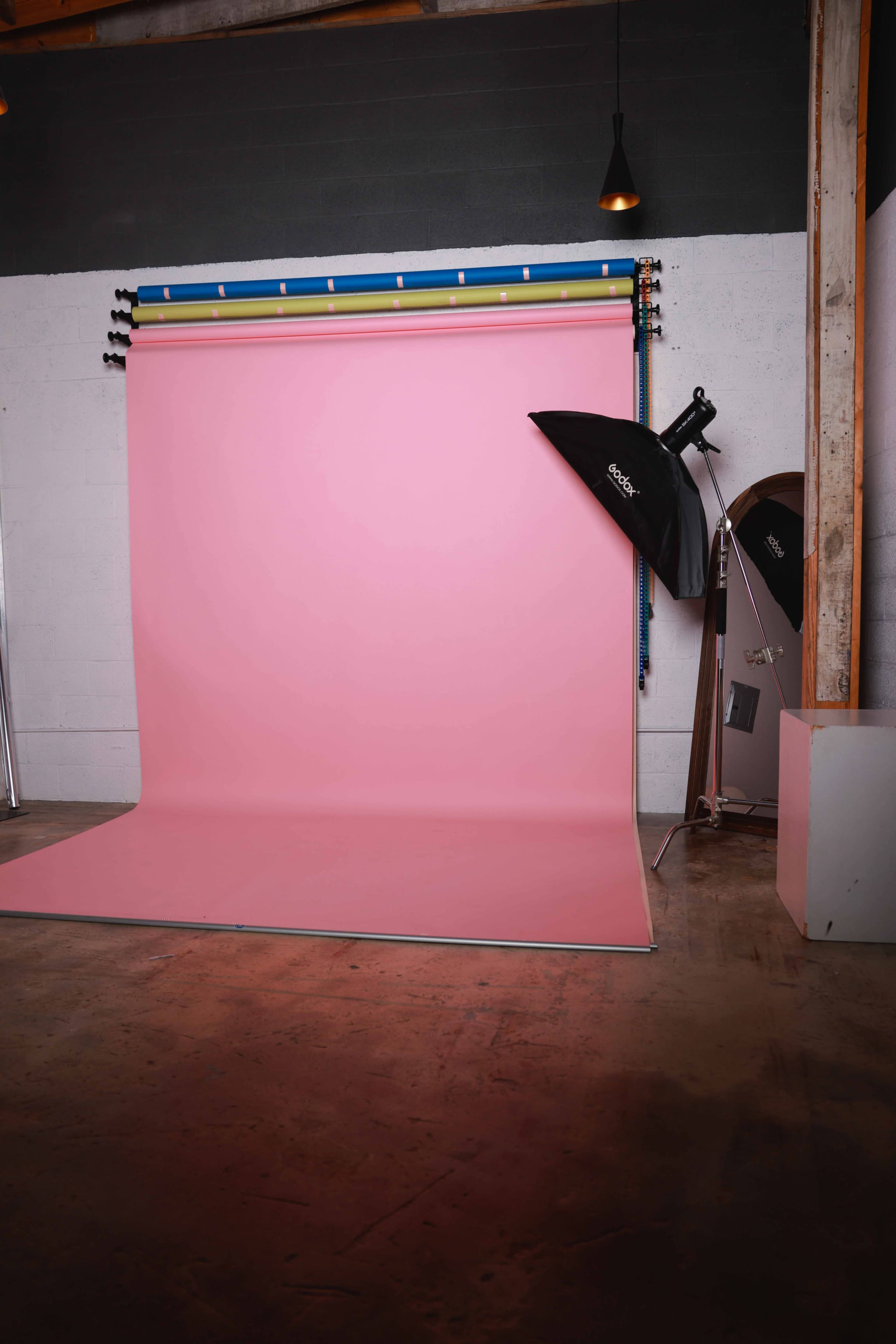 A photography studio features a pink backdrop with studio lighting equipment and a mirror.