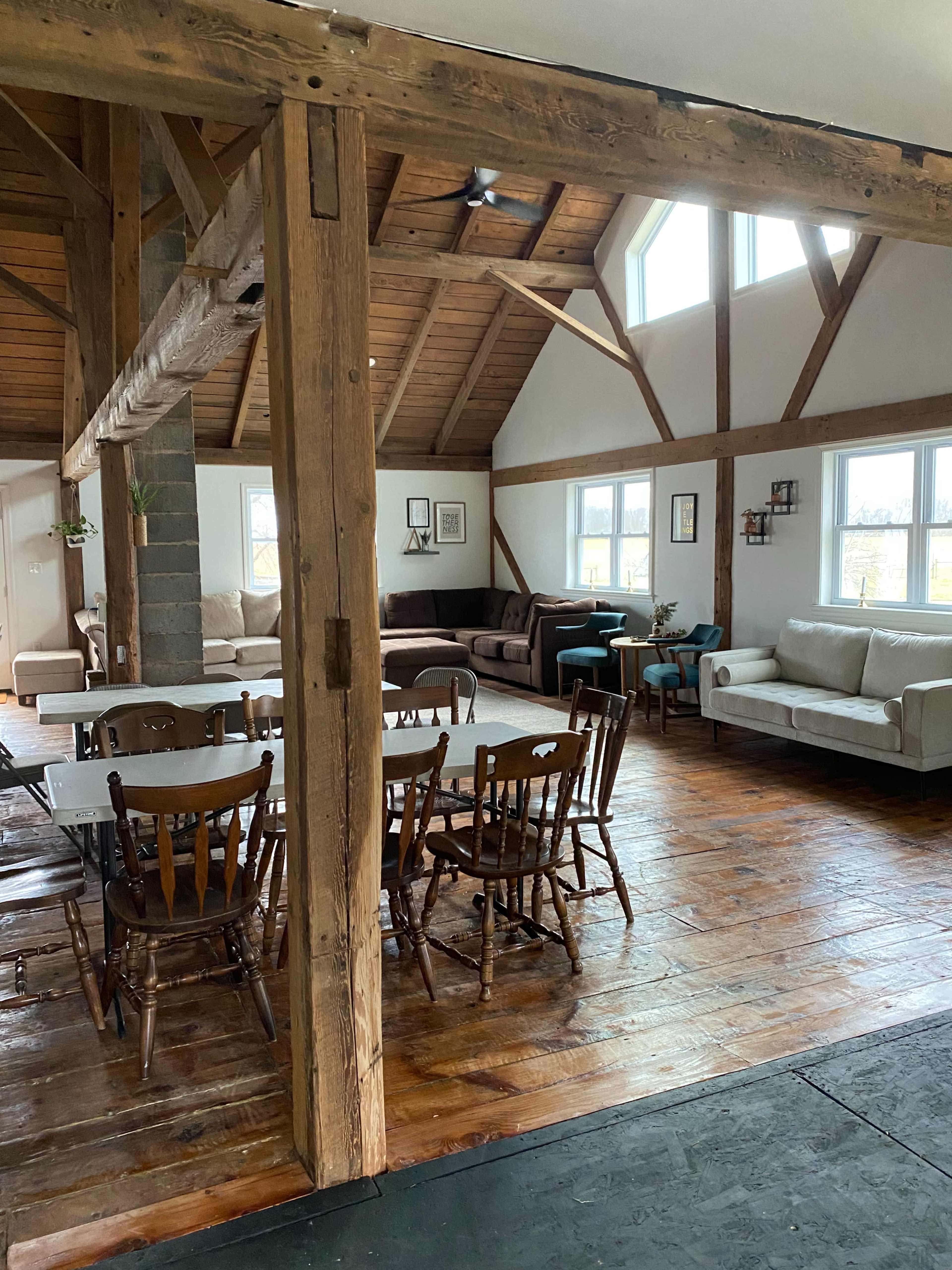 A spacious open-plan living area with wooden beams, a dining table surrounded by chairs, and various seating arrangements including couches.