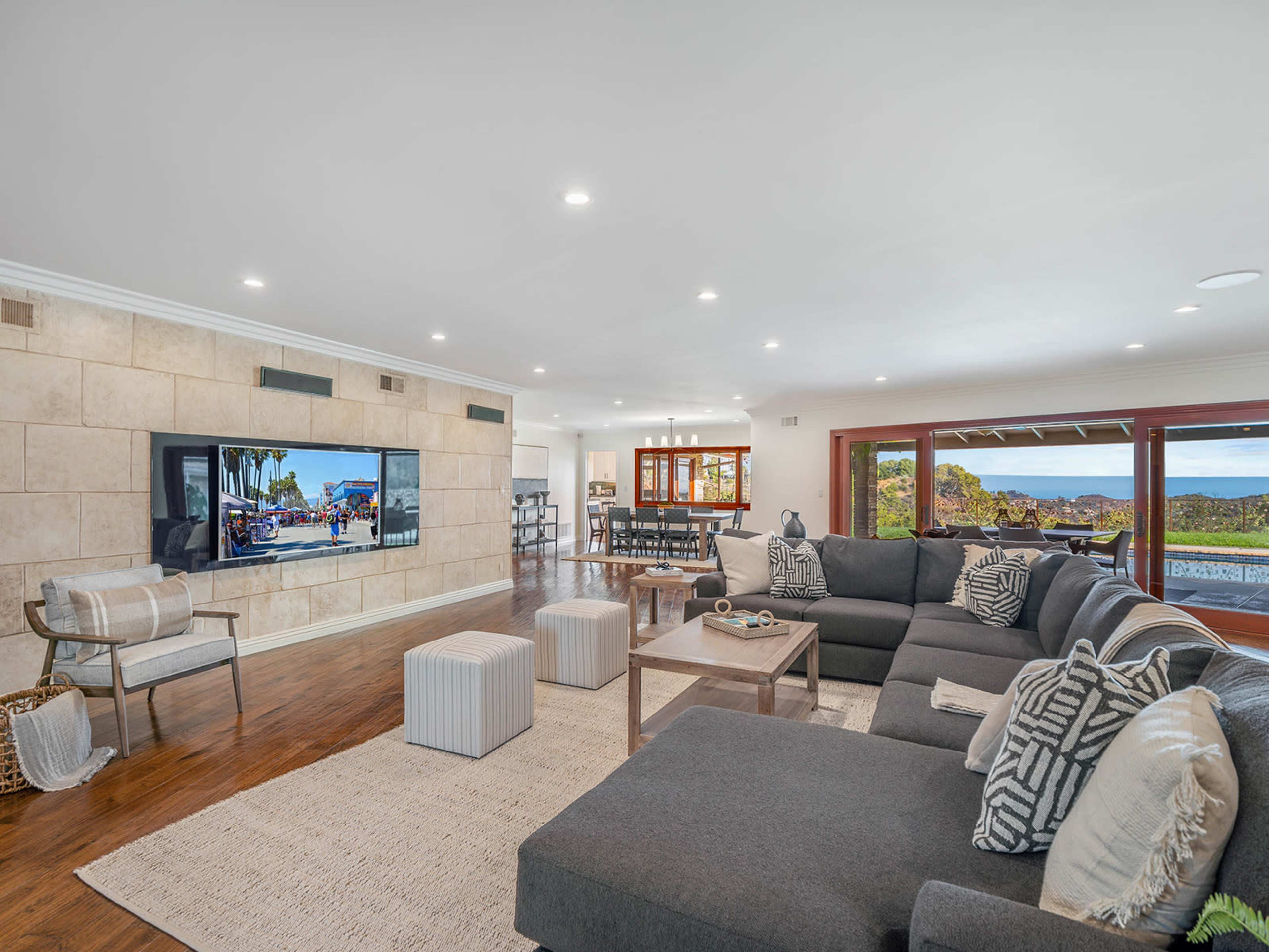 A spacious living room with a large sectional sofa, a coffee table, and a mounted television displaying a scenic view.