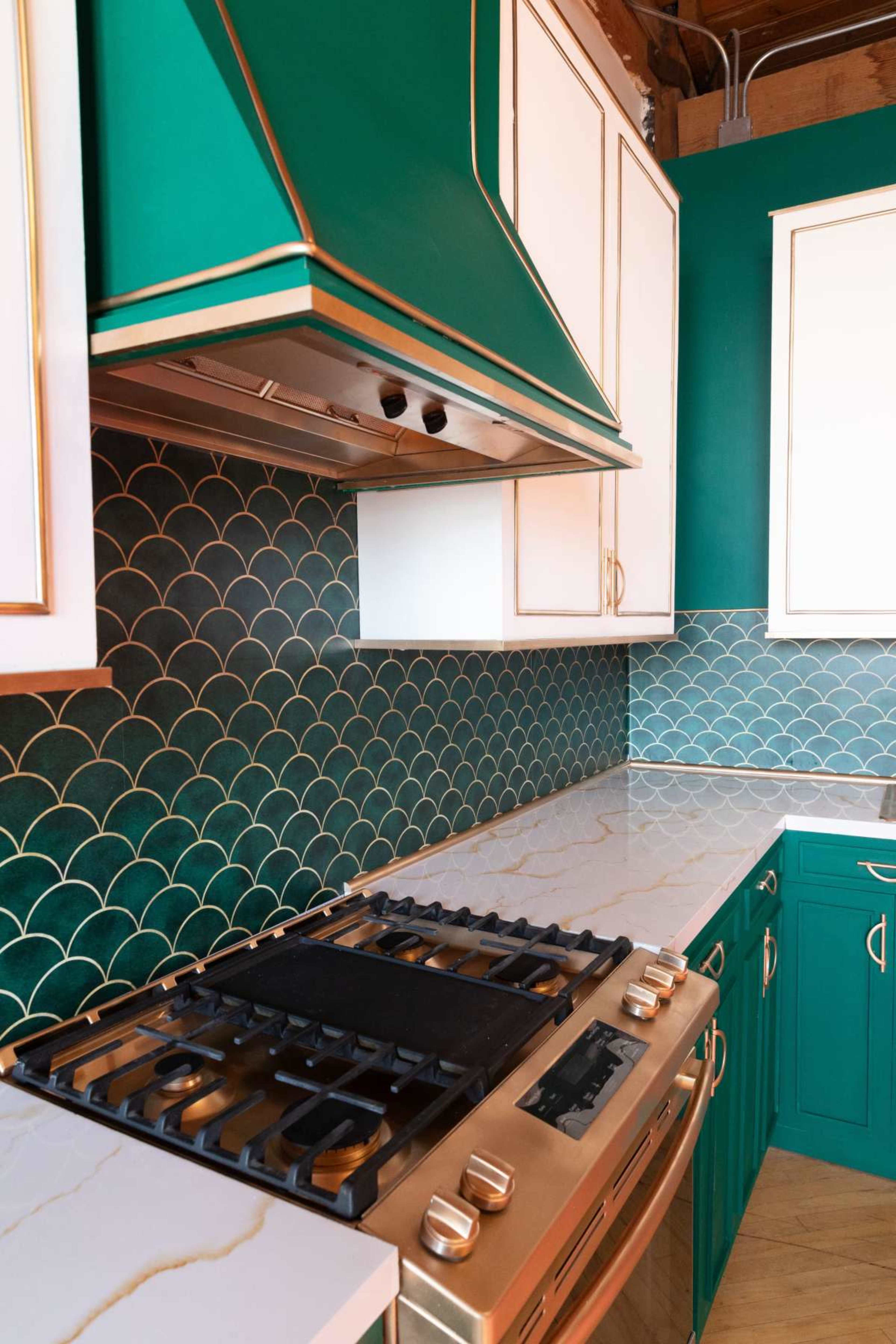 The image features a kitchen with teal cabinetry, a gold-accented range hood, and a backsplash of green scalloped tiles.
