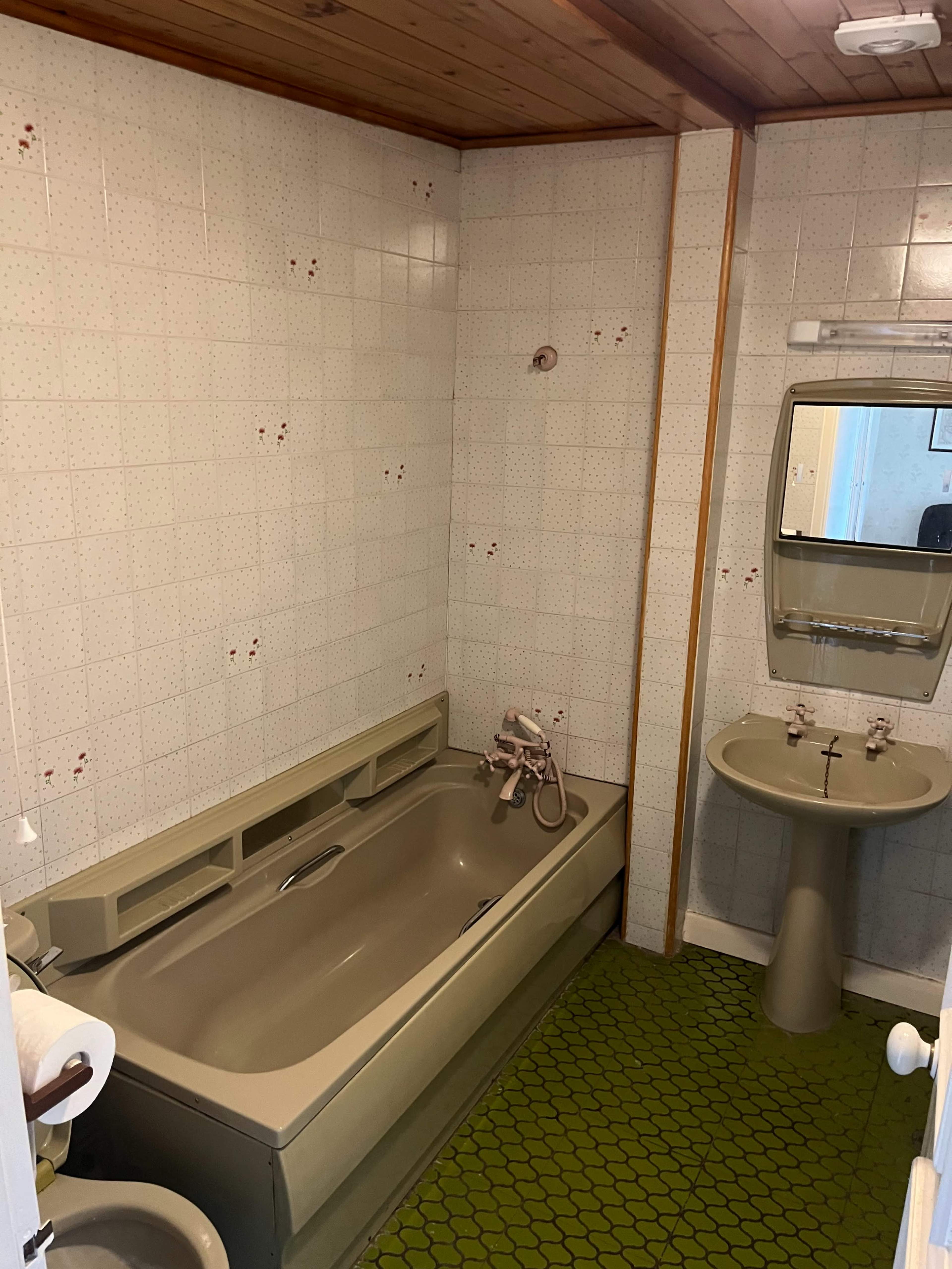 A small bathroom featuring a bathtub, sink, and tiled walls with a green patterned floor.