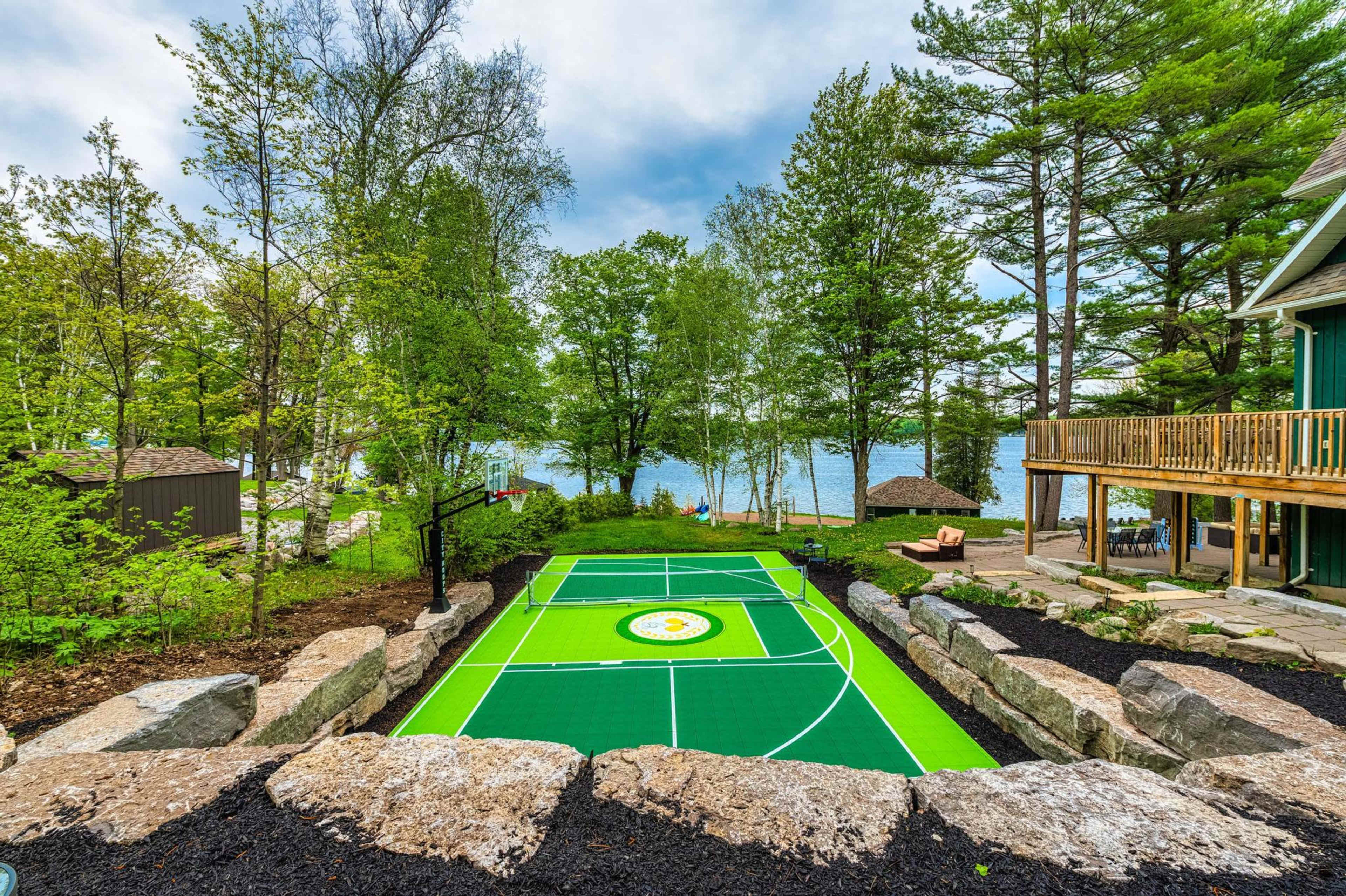 A vibrant green sporting court surrounded by natural landscaping, with a lake and trees in the background.