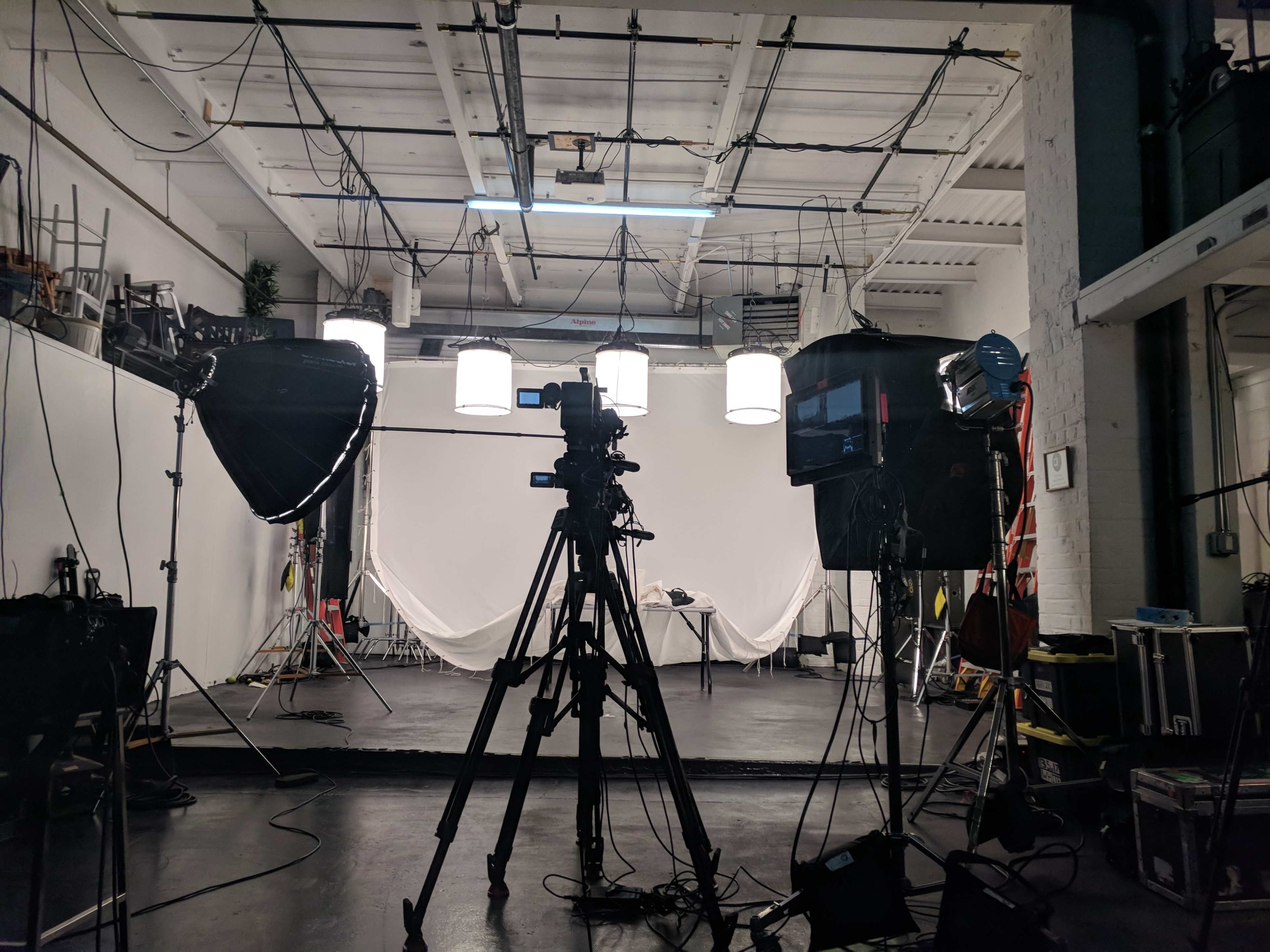 A photography studio equipped with lights, a video camera on a tripod, and a blank backdrop.