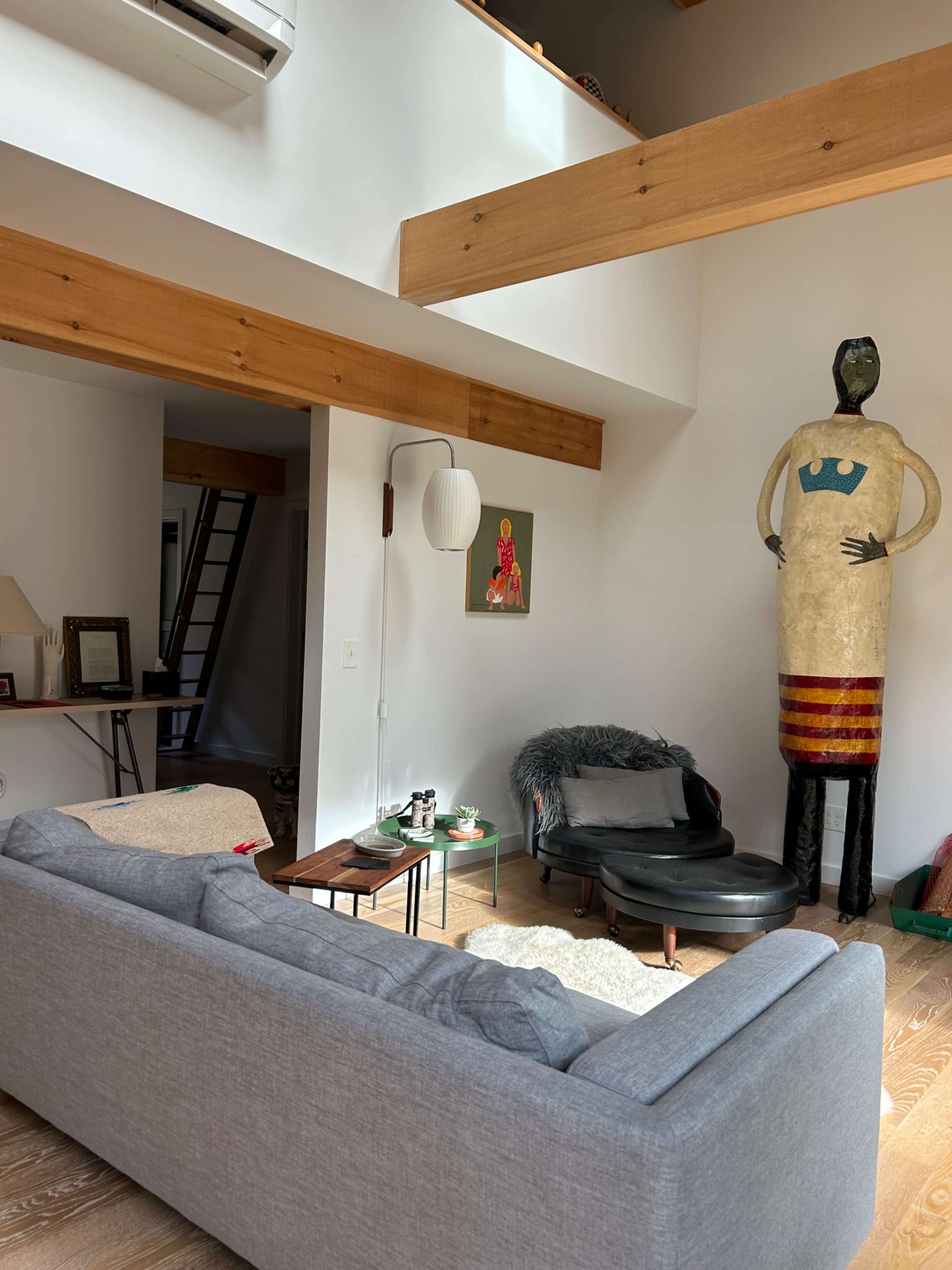 A modern living room with a gray sofa, a small wooden table, and a large decorative figure against a white wall.
