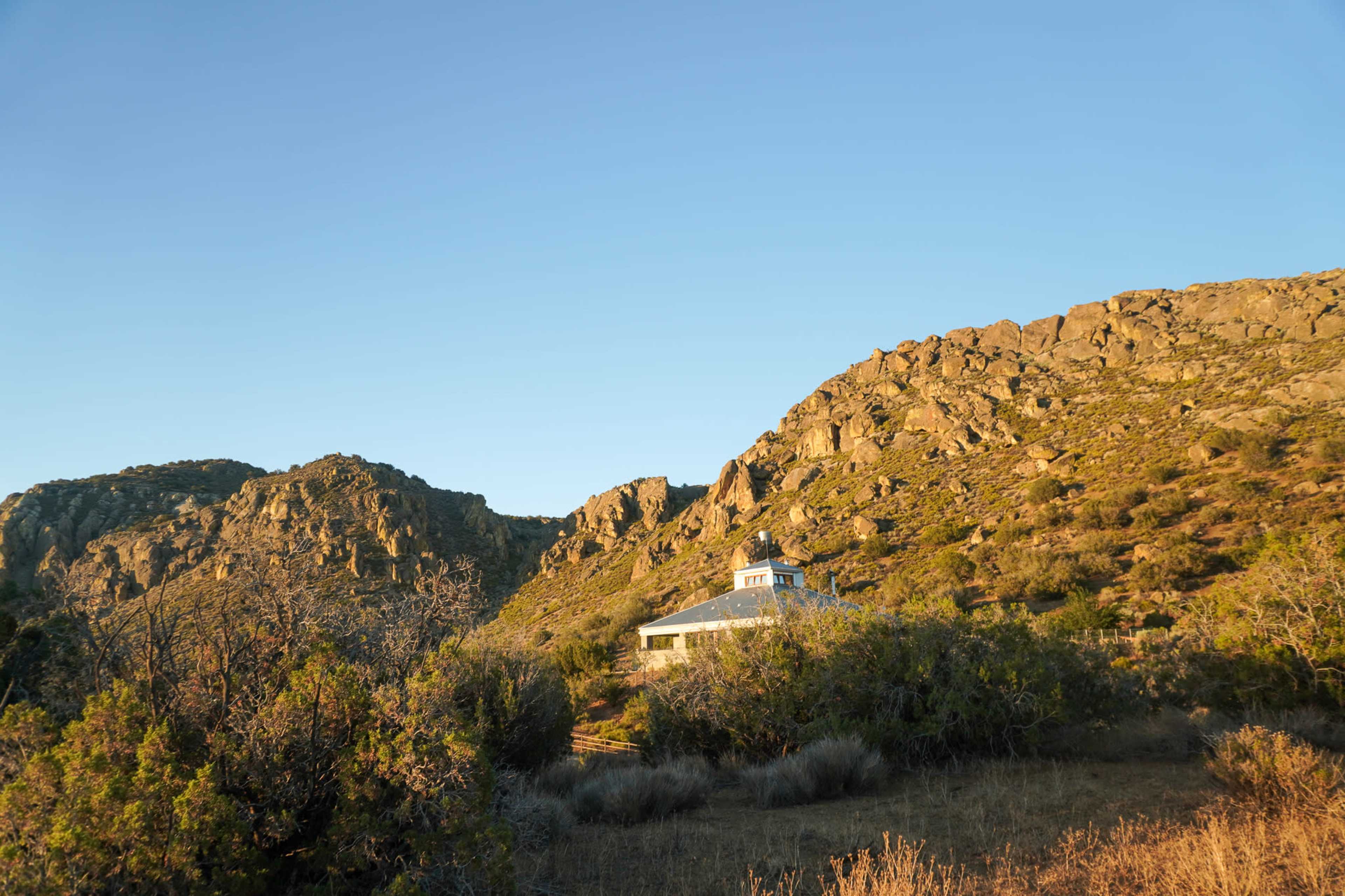 A white building is situated near rocky hills under a clear blue sky.