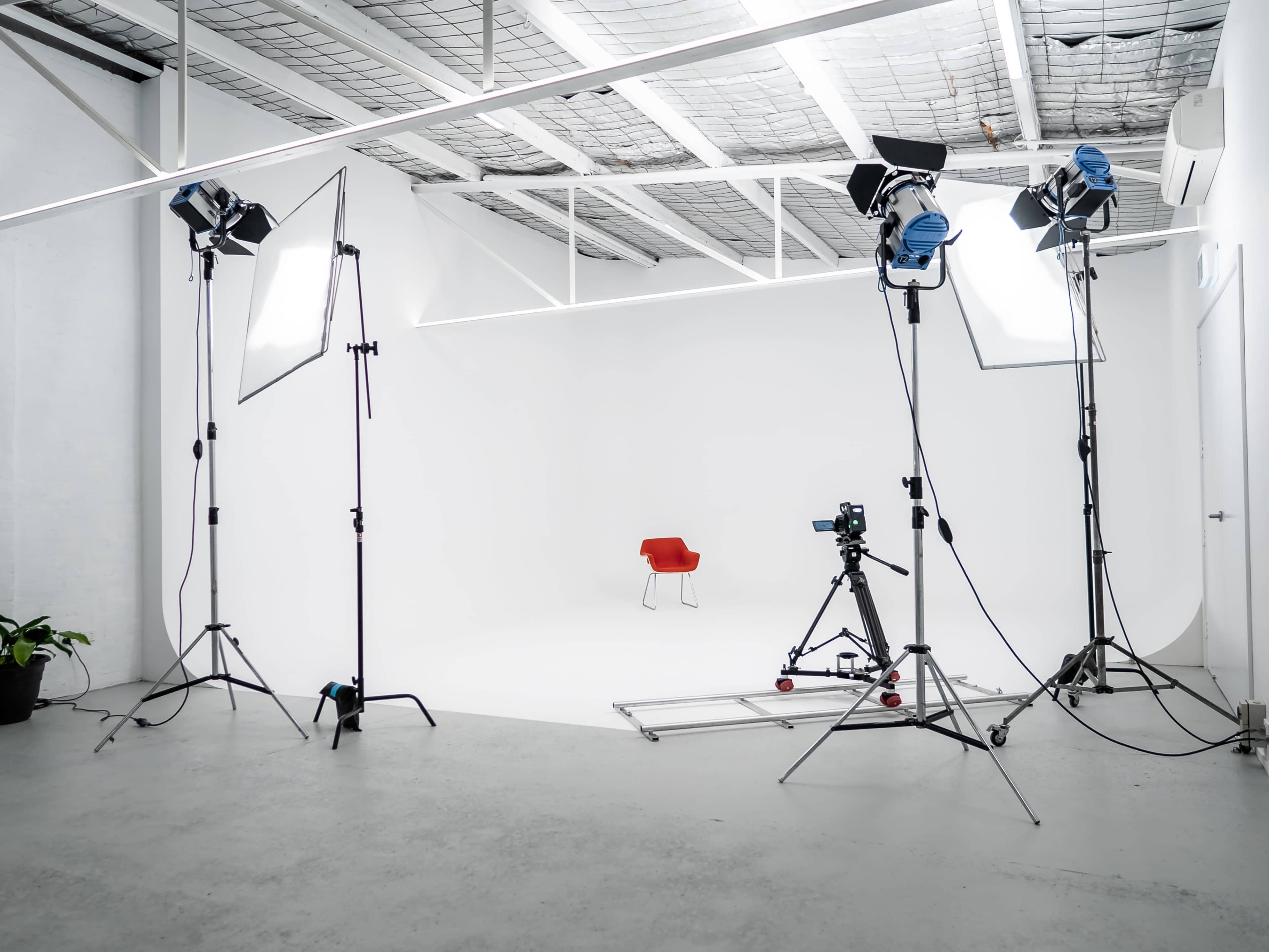 A minimalistic photo studio features a red chair positioned at the center, surrounded by lighting equipment and a camera on a track.