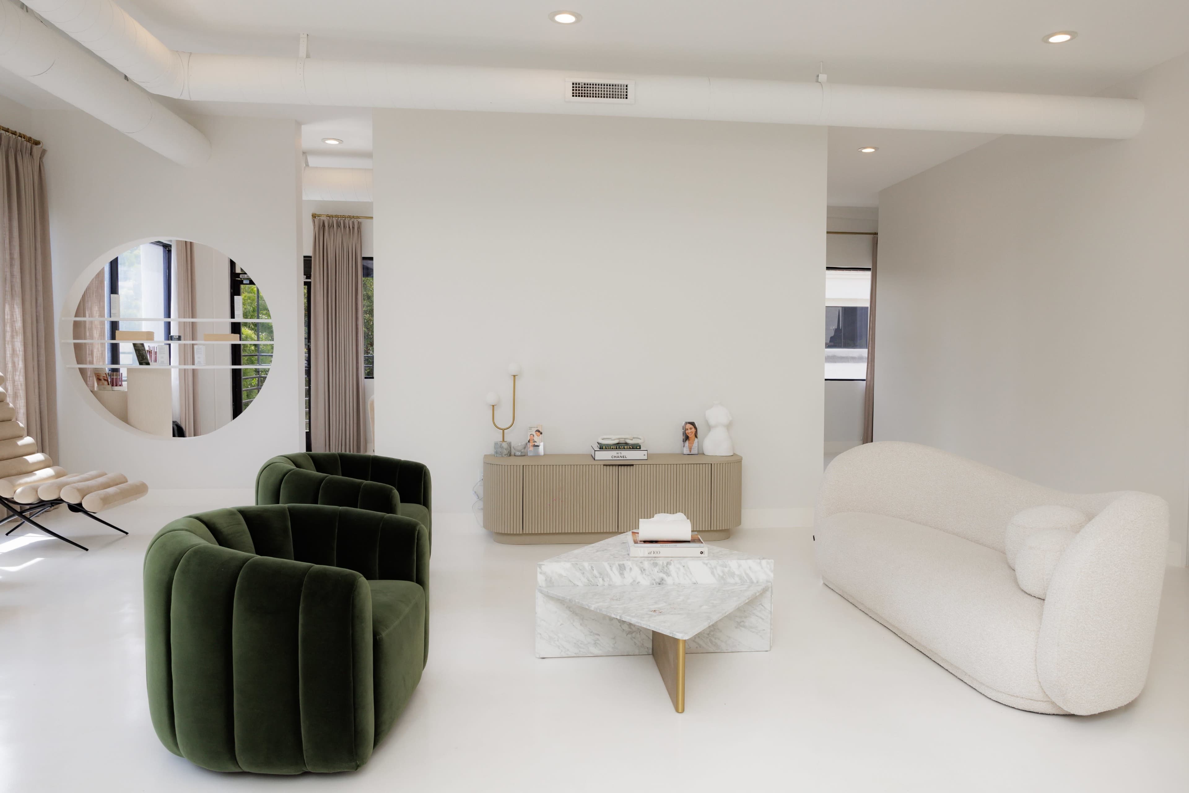 The image shows a contemporary living space featuring two plush sofas, a marble coffee table, and a round mirror on the wall.