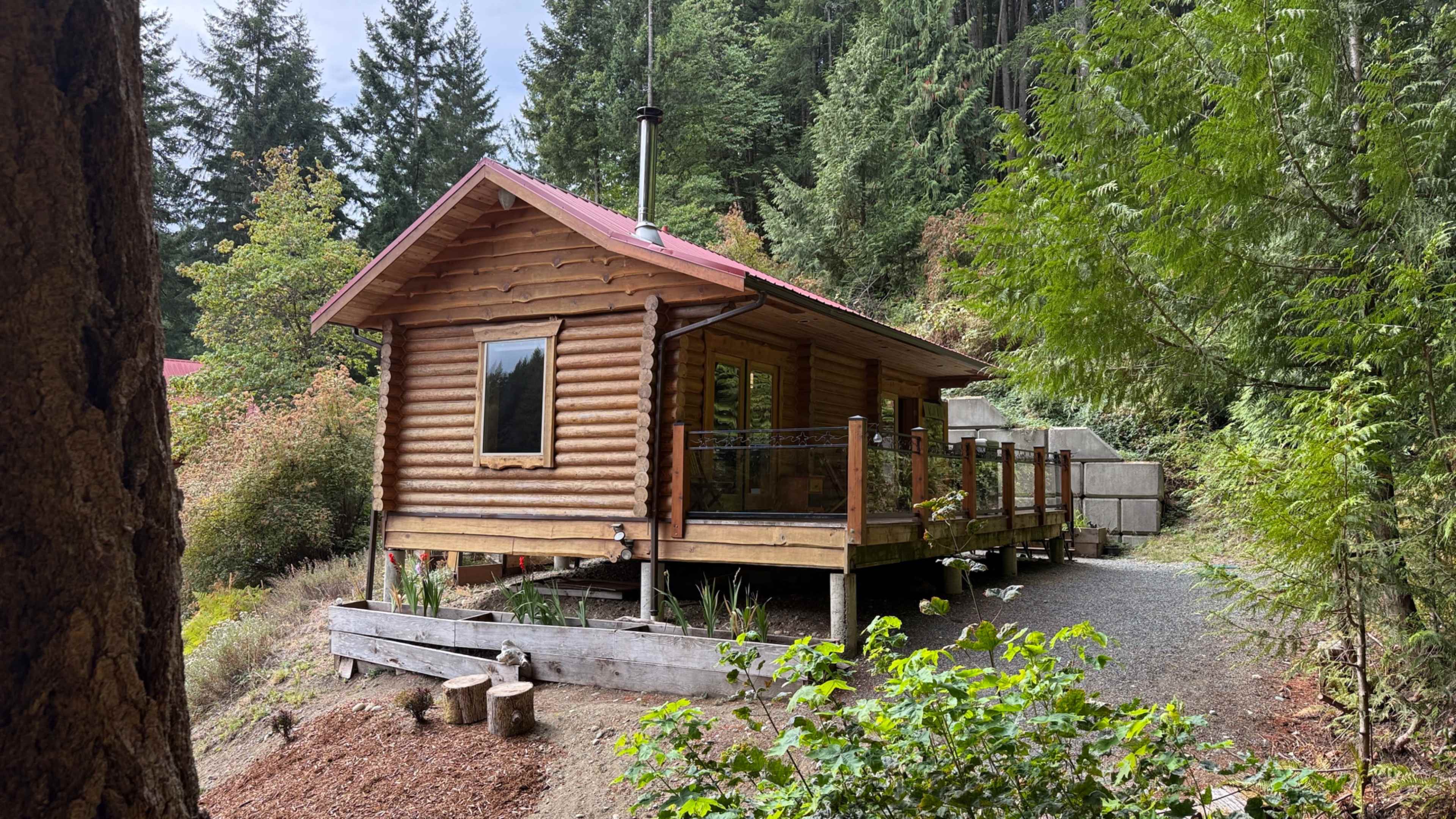 The image shows a wooden cabin with a red roof situated among trees on a sloped landscape.