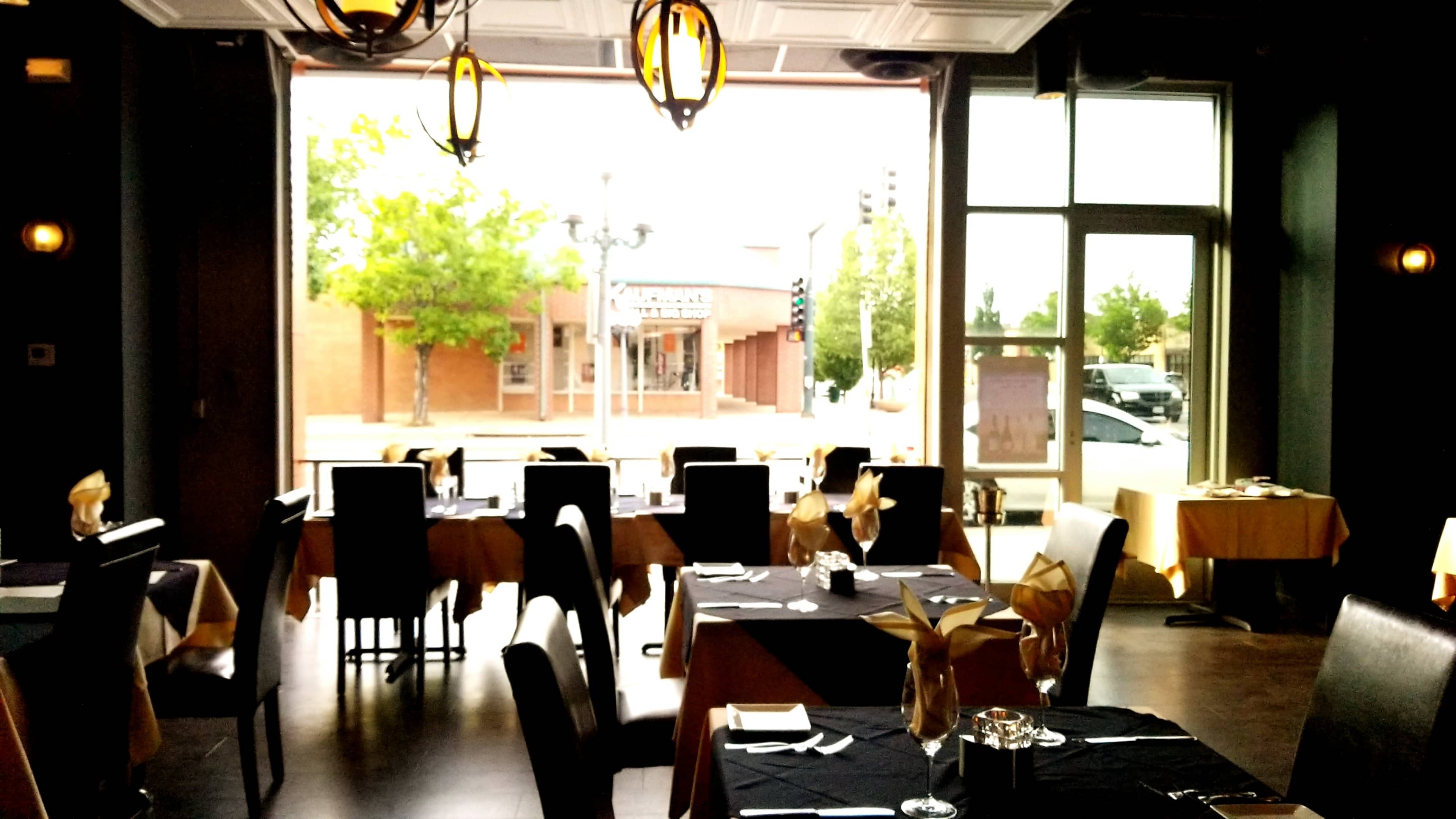 The image shows a restaurant interior featuring black tables with gold accents and a large window displaying an urban street scene outside.