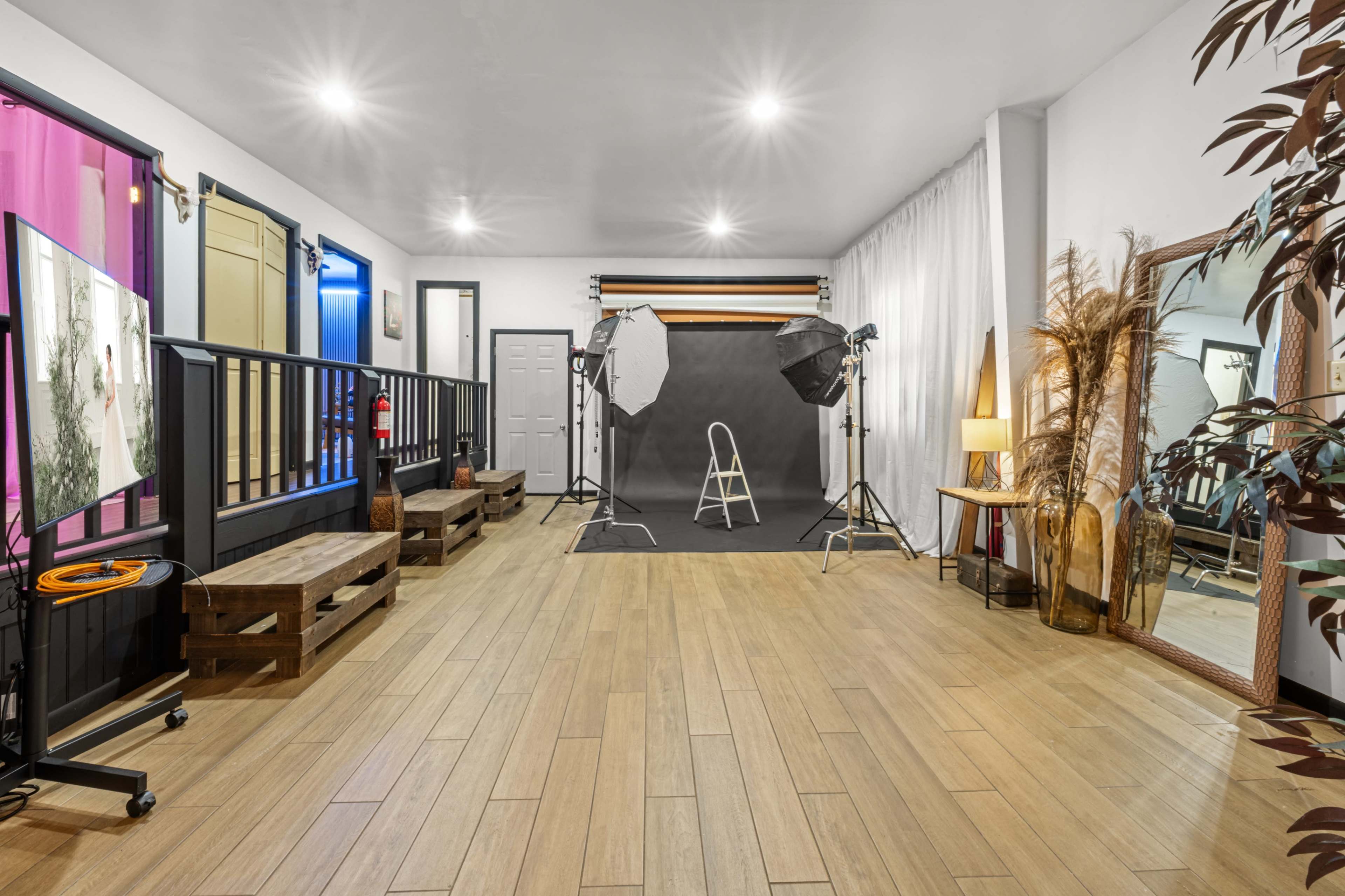 The image shows a photography studio with a black backdrop, lighting equipment, and various props arranged around a wooden floor.