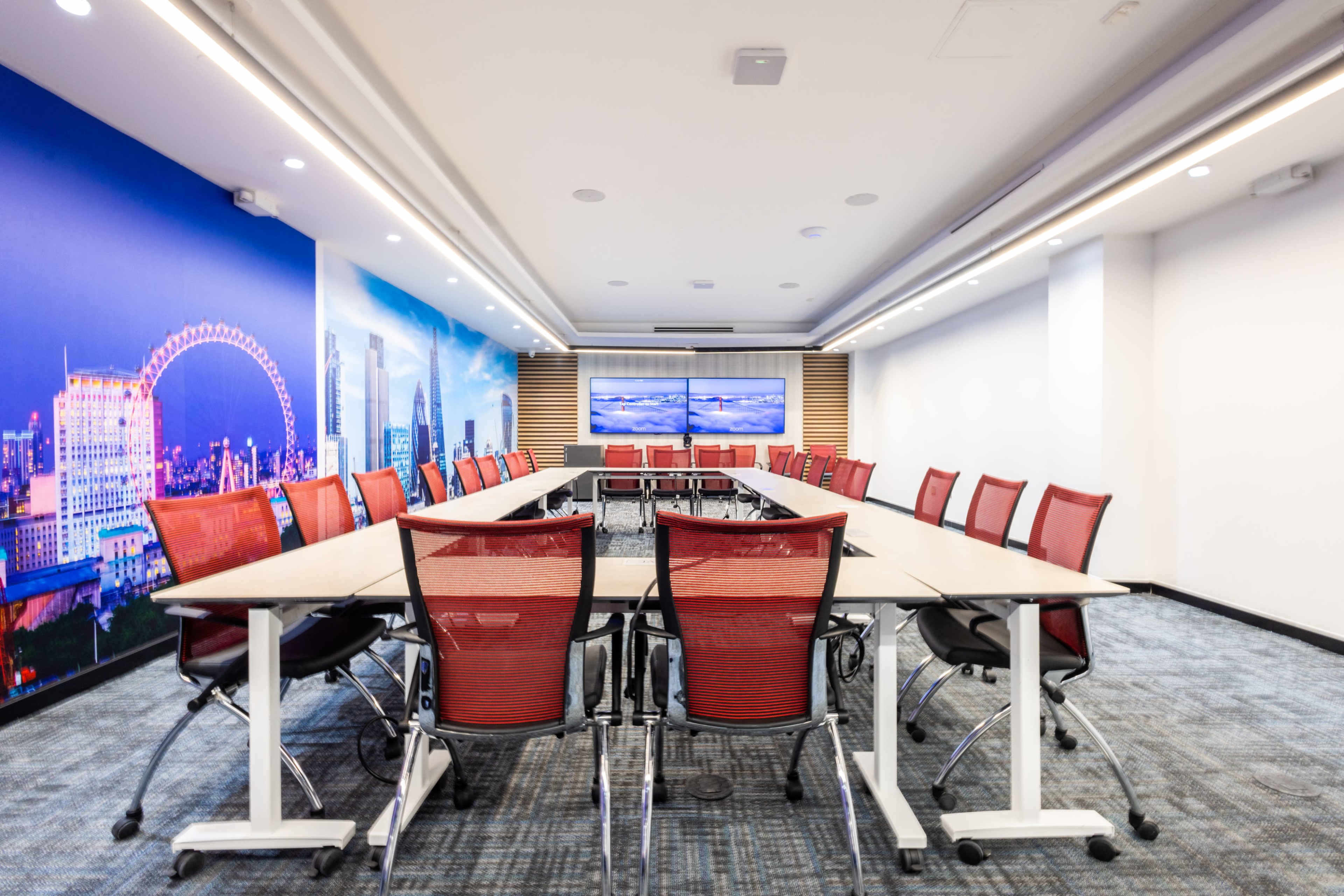 A modern conference room with a large table surrounded by red chairs and a backdrop featuring a cityscape.