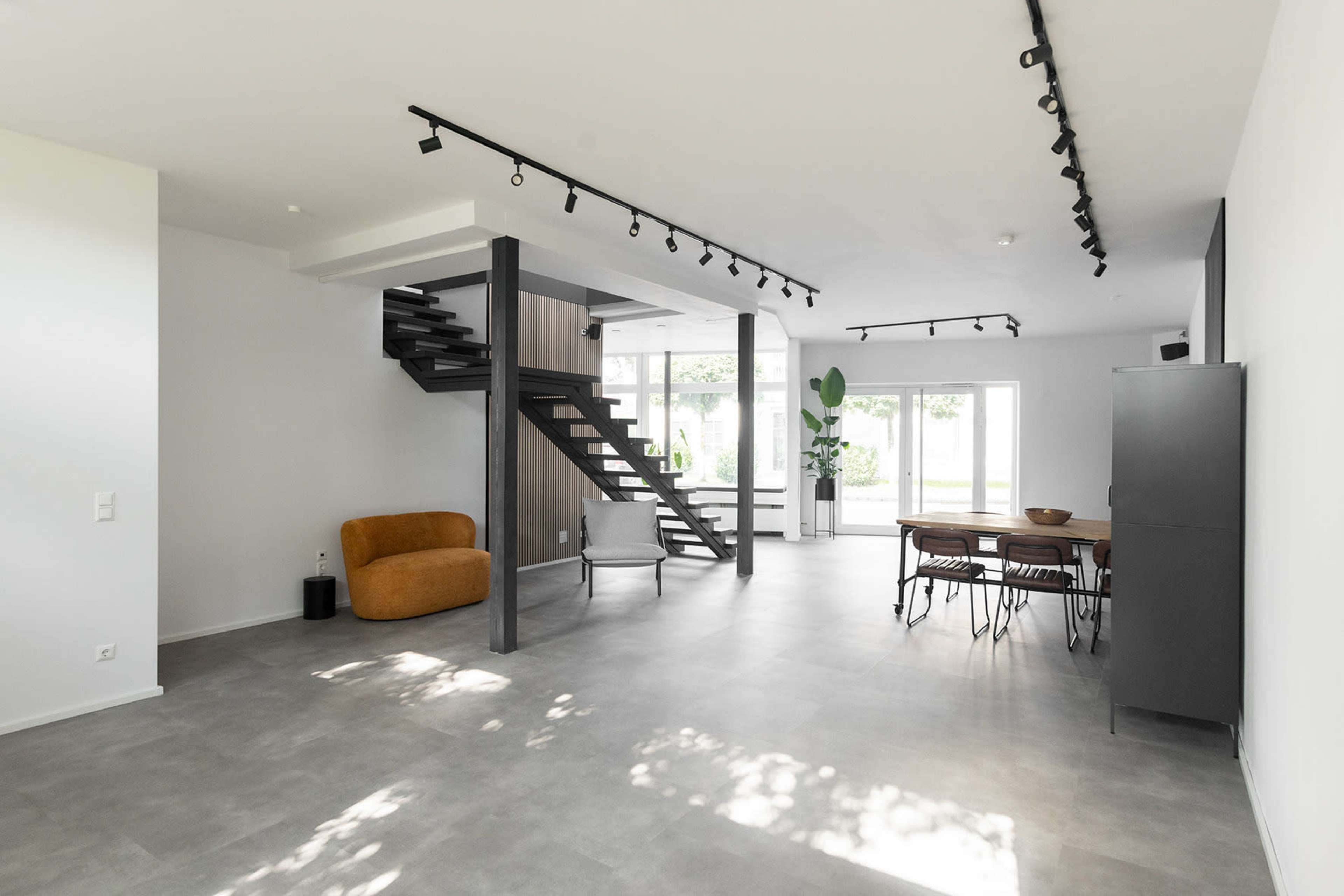 The image shows a modern, open-concept living space with a staircase, large windows, and a dining area.