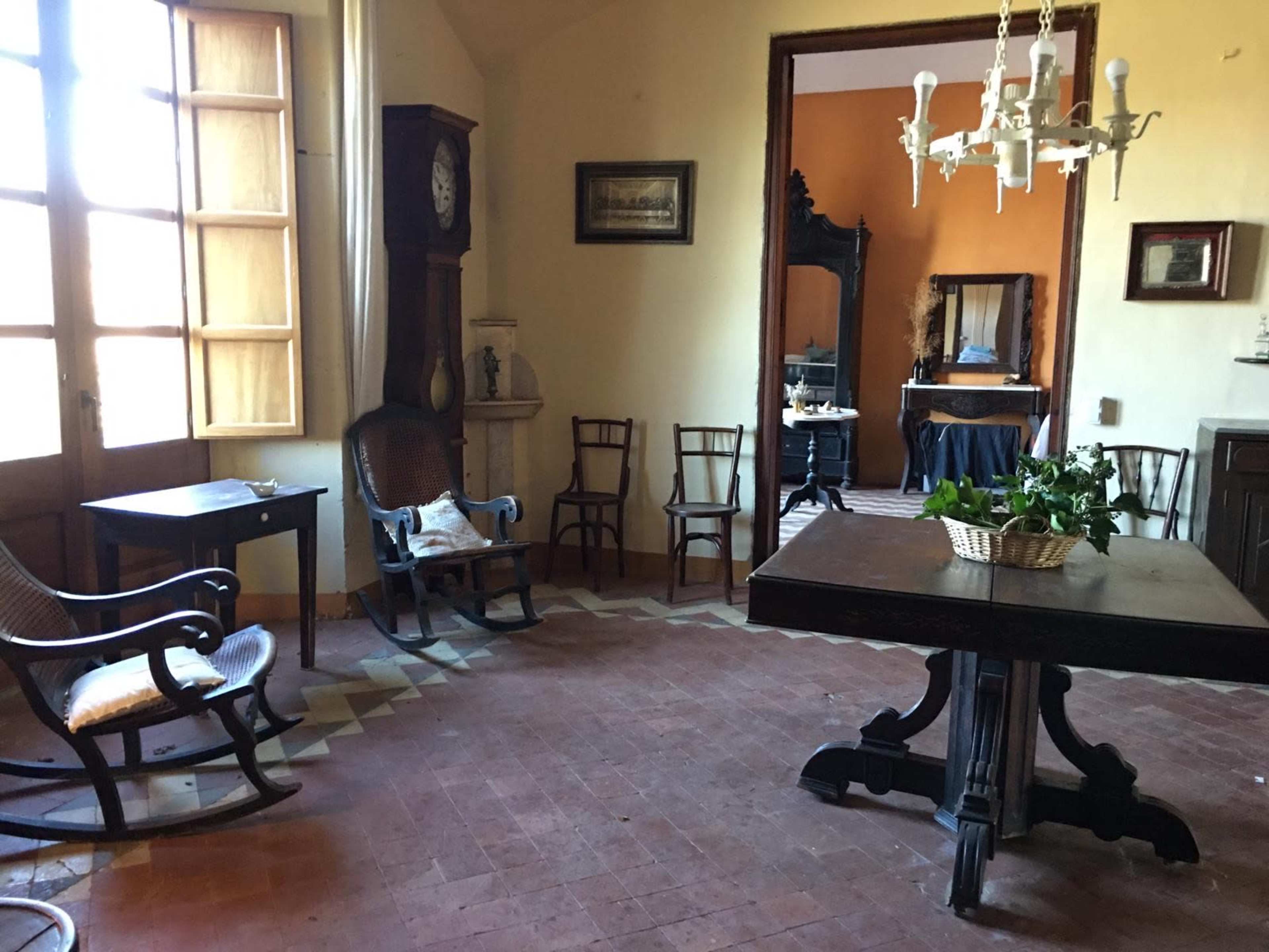 An unfurnished room with a wooden table, chairs, and large windows allowing natural light.