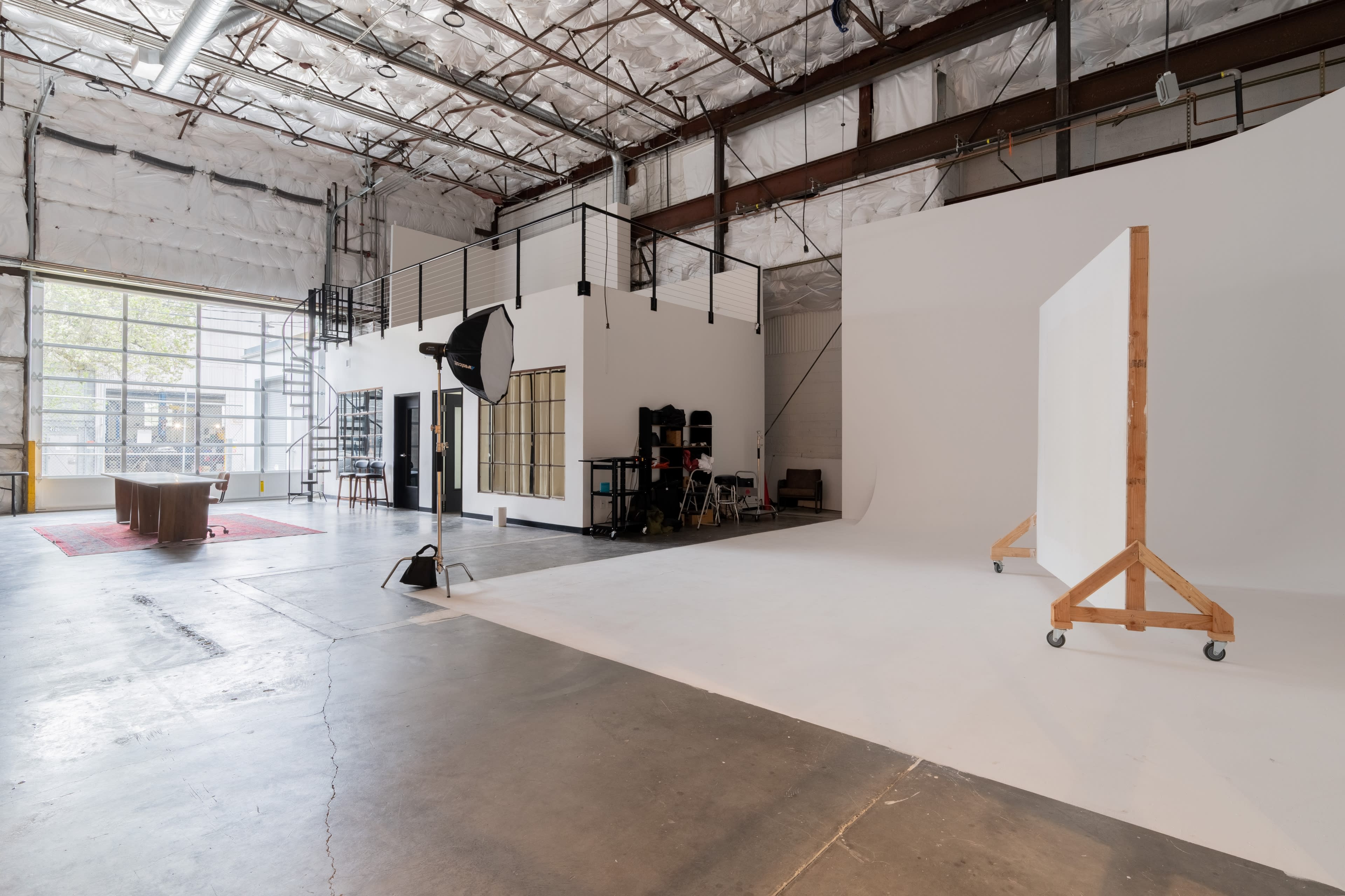 The image shows a spacious photography studio with large windows, various equipment, and a backdrop setup.