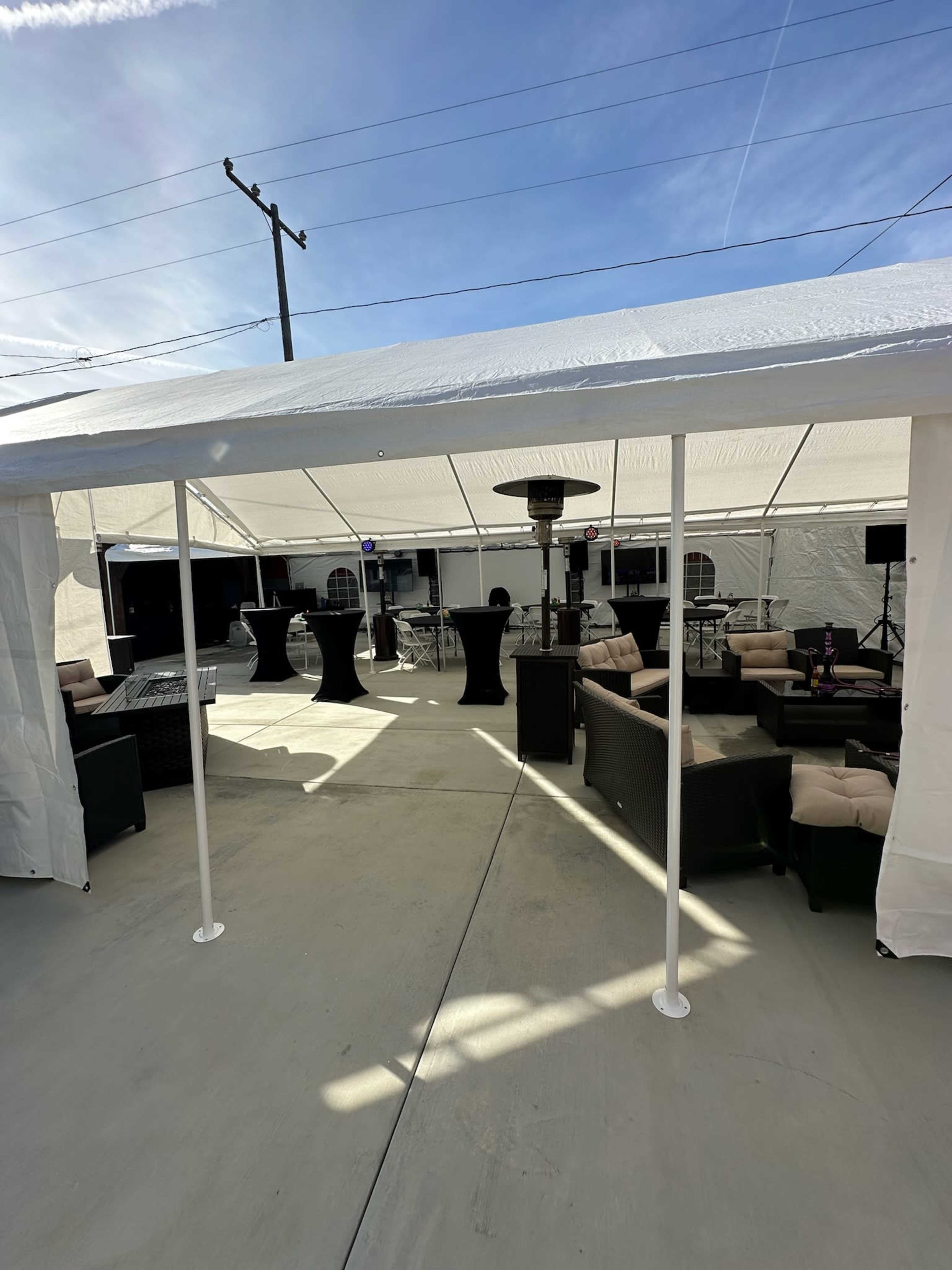 A white tented area features black cocktail tables and upholstered seating, with a heater visible in the background.