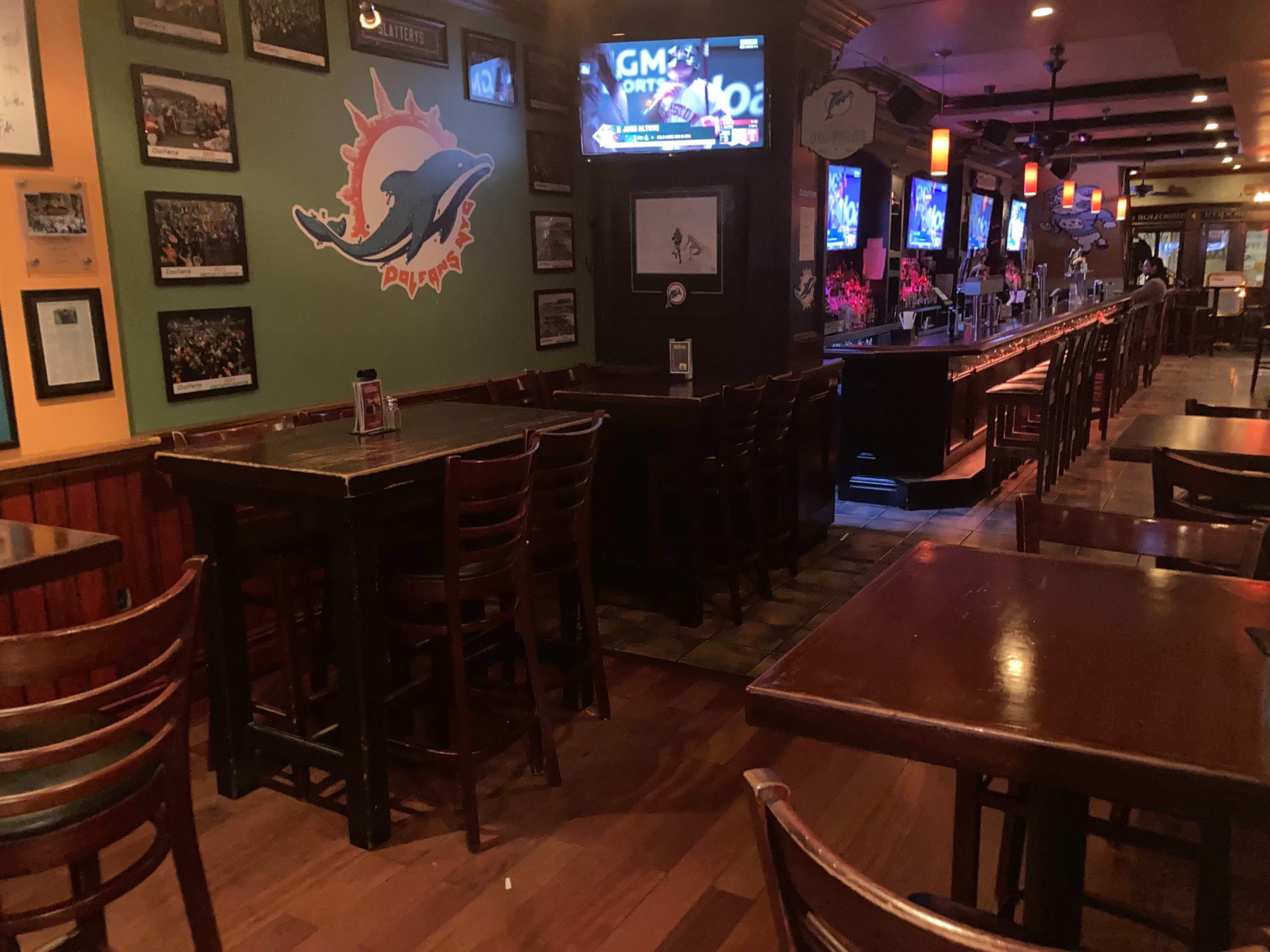 An empty bar with wooden tables and chairs, featuring multiple televisions mounted on the walls.