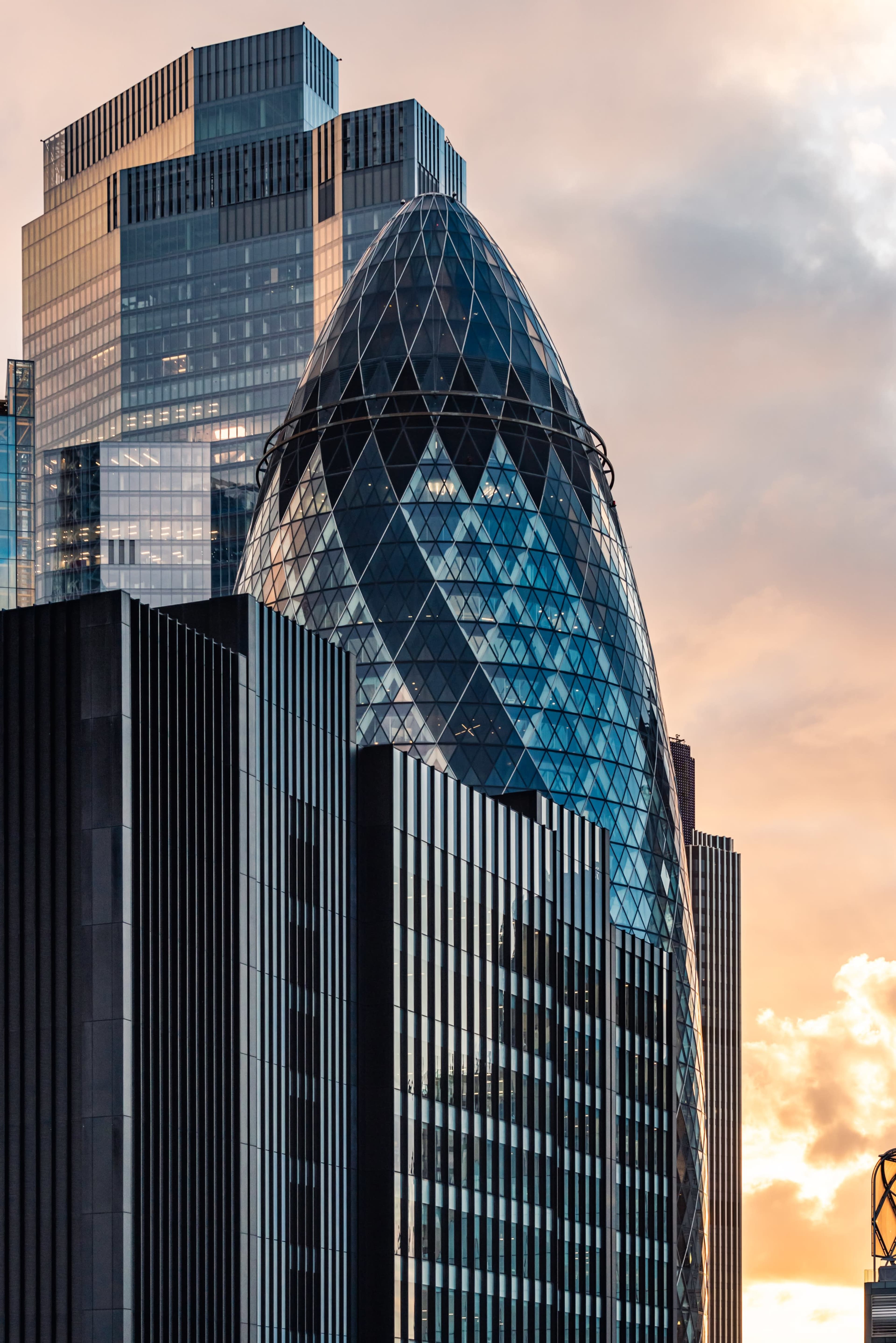 The image shows a modern skyscraper with a distinctive egg-shaped dome atop a series of dark, vertical structures, set against a colorful sunset sky.