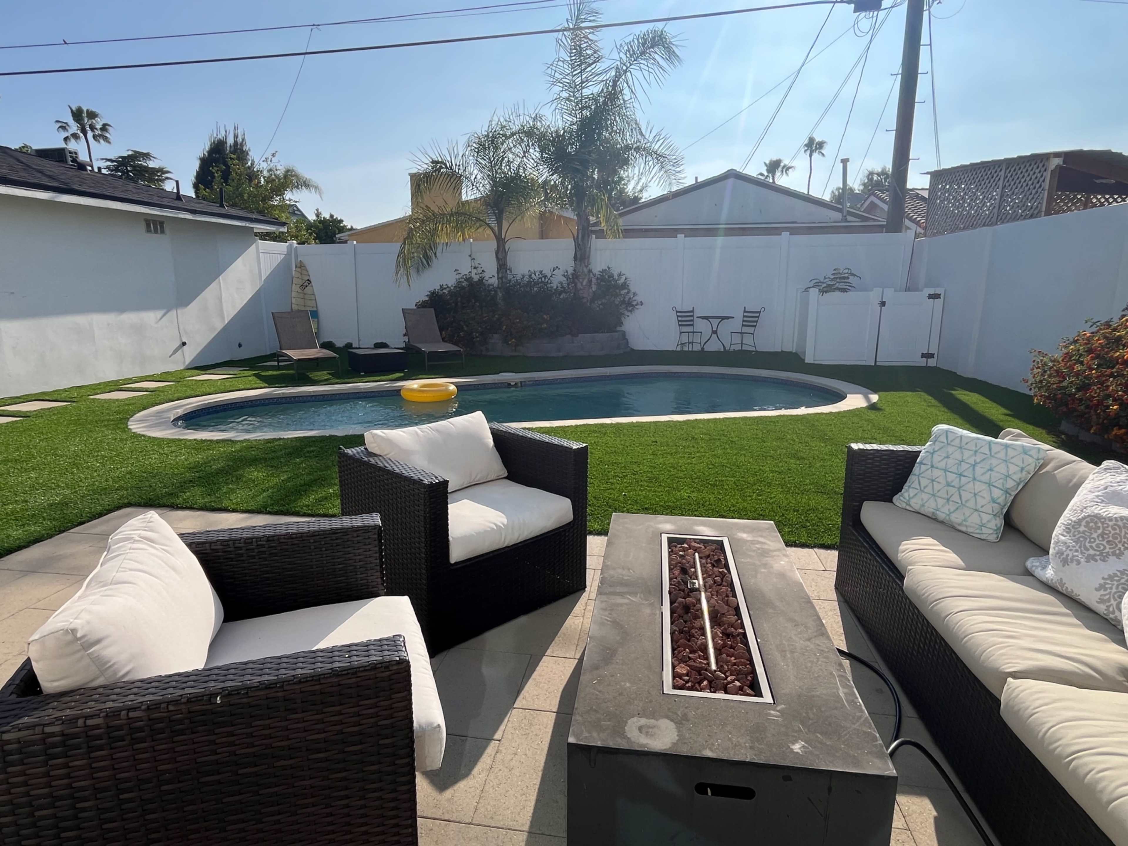 A backyard with a swimming pool, lounge chairs, and outdoor seating arranged around a fire pit on a patio.