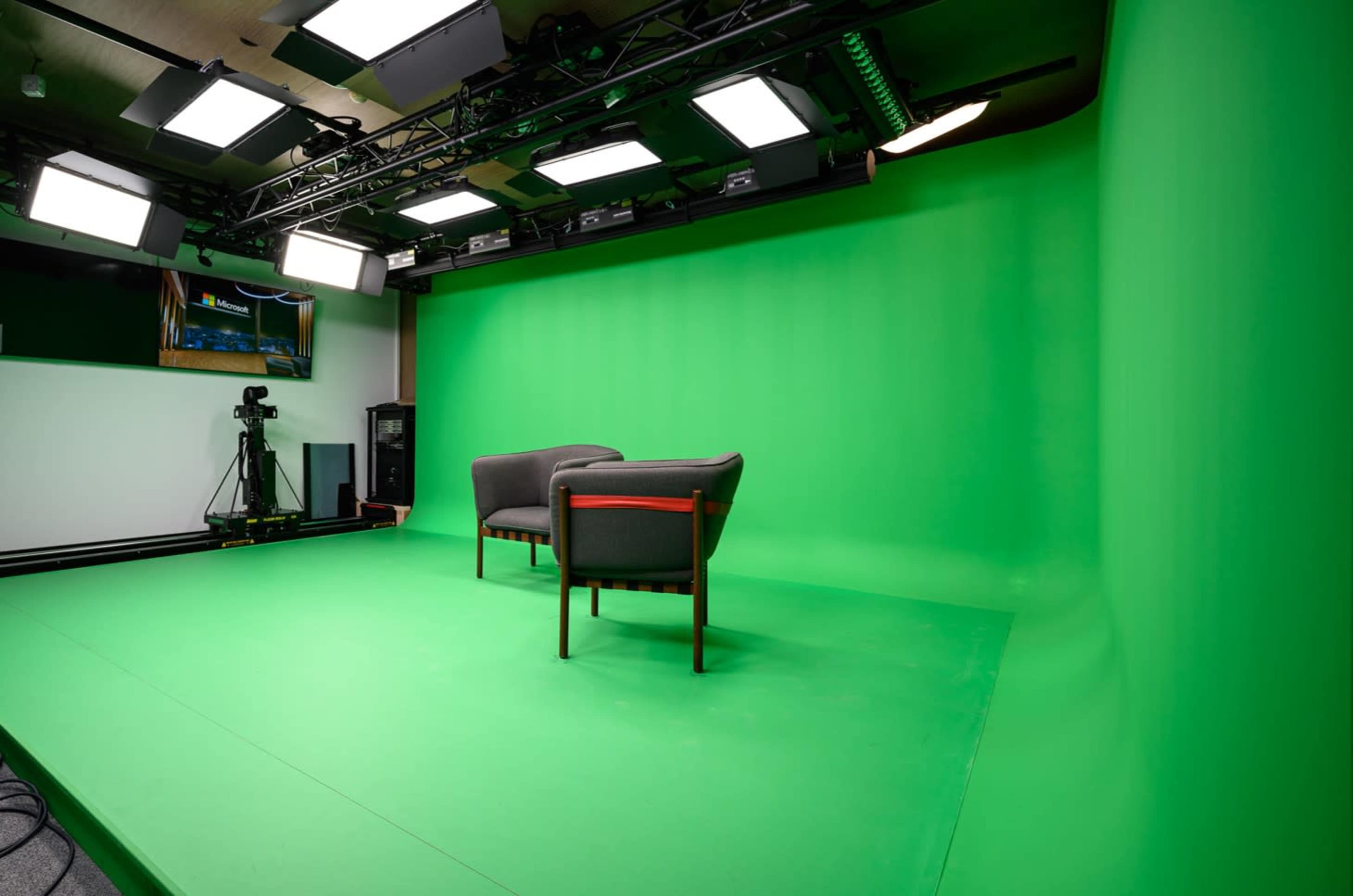 The image shows a studio setup featuring two chairs on a bright green backdrop, with multiple overhead lights aimed at the seating area.