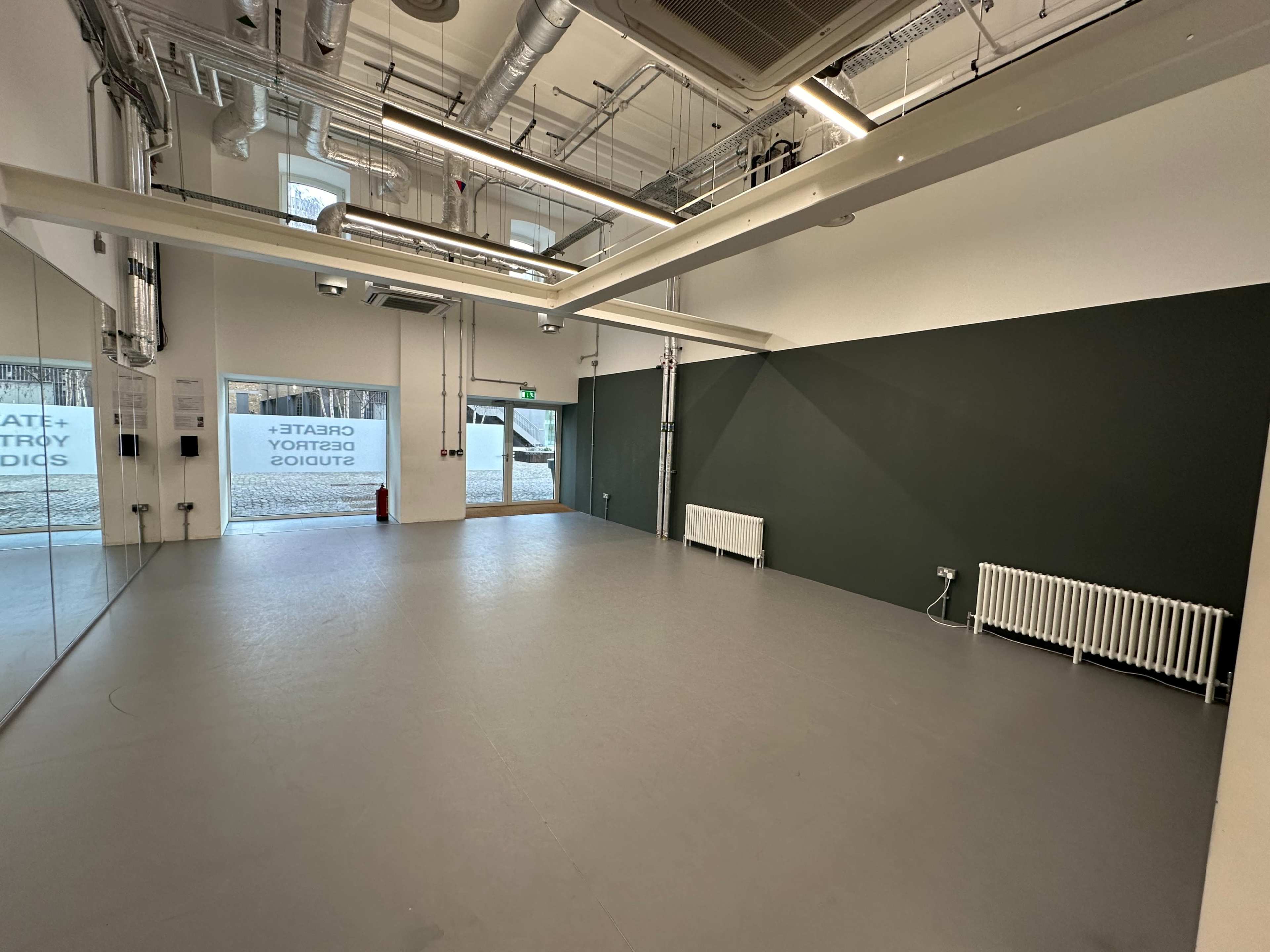 The image shows a spacious, well-lit, empty studio with a green accent wall and large windows along one side.