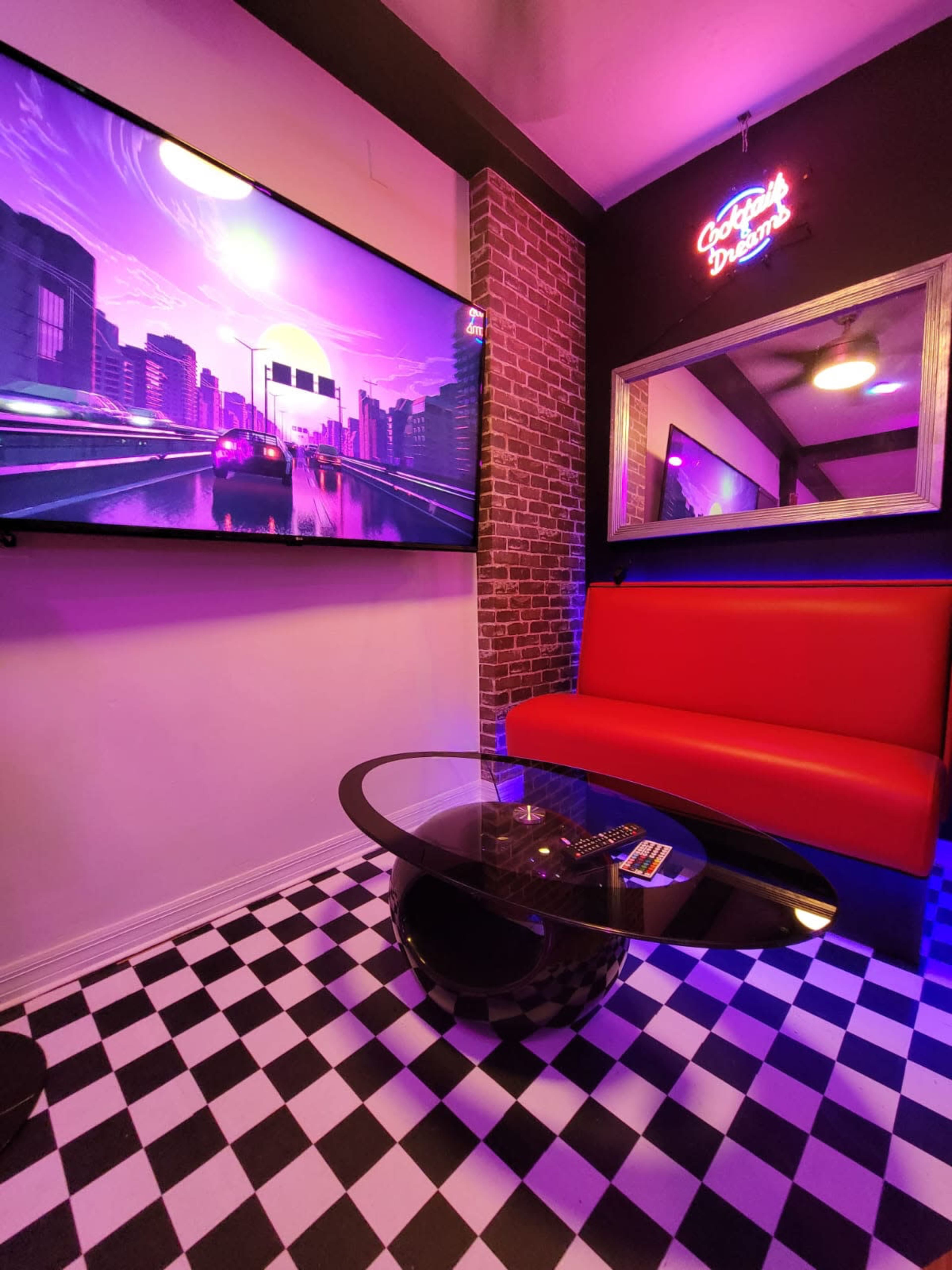 A room with a large television displaying a cityscape, a red bench-style seat, a circular glass table, and a checkered black-and-white floor.