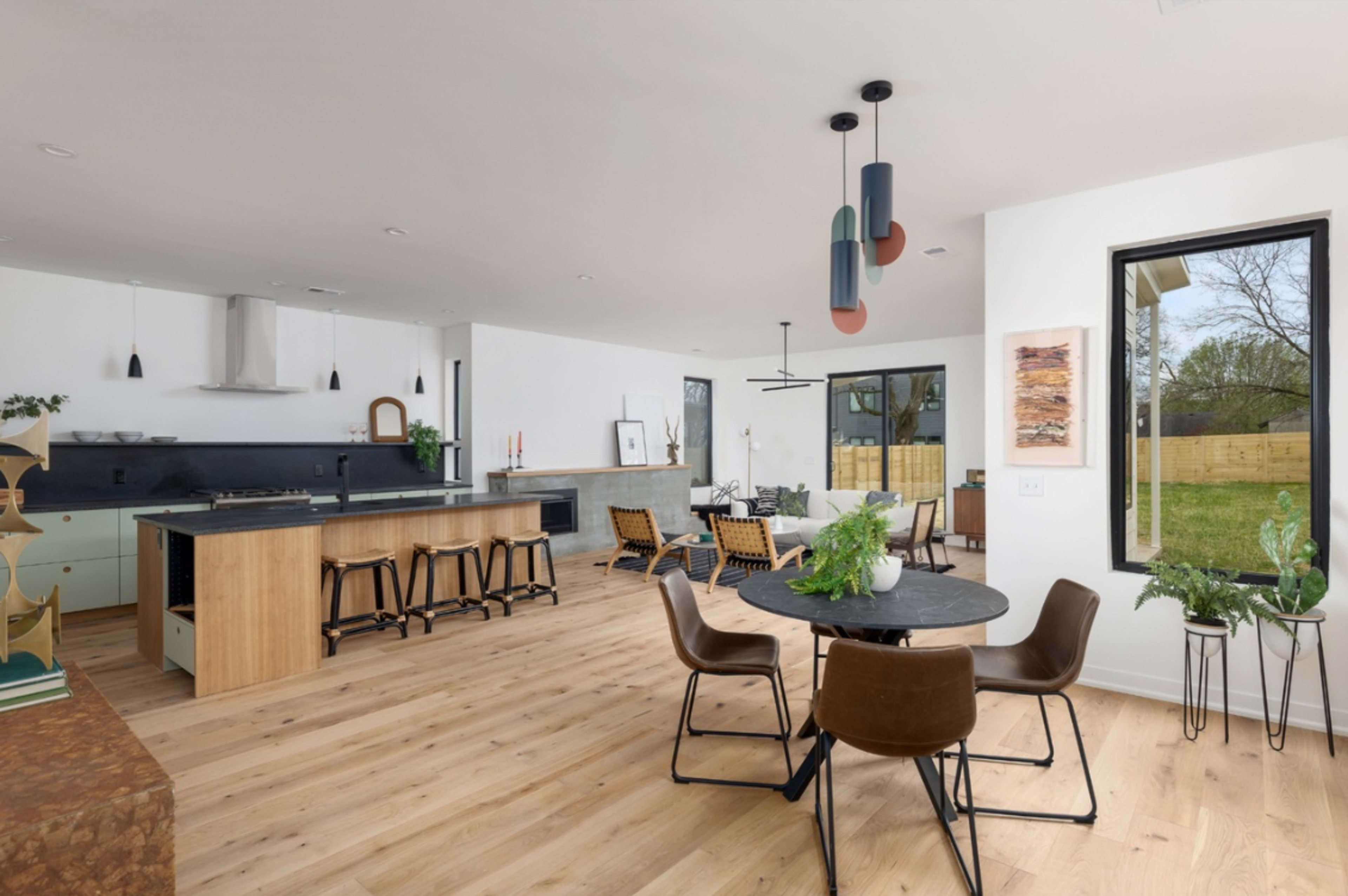 The image shows a modern open-concept living space featuring a kitchen, dining area, and seating area with large windows and wooden flooring.