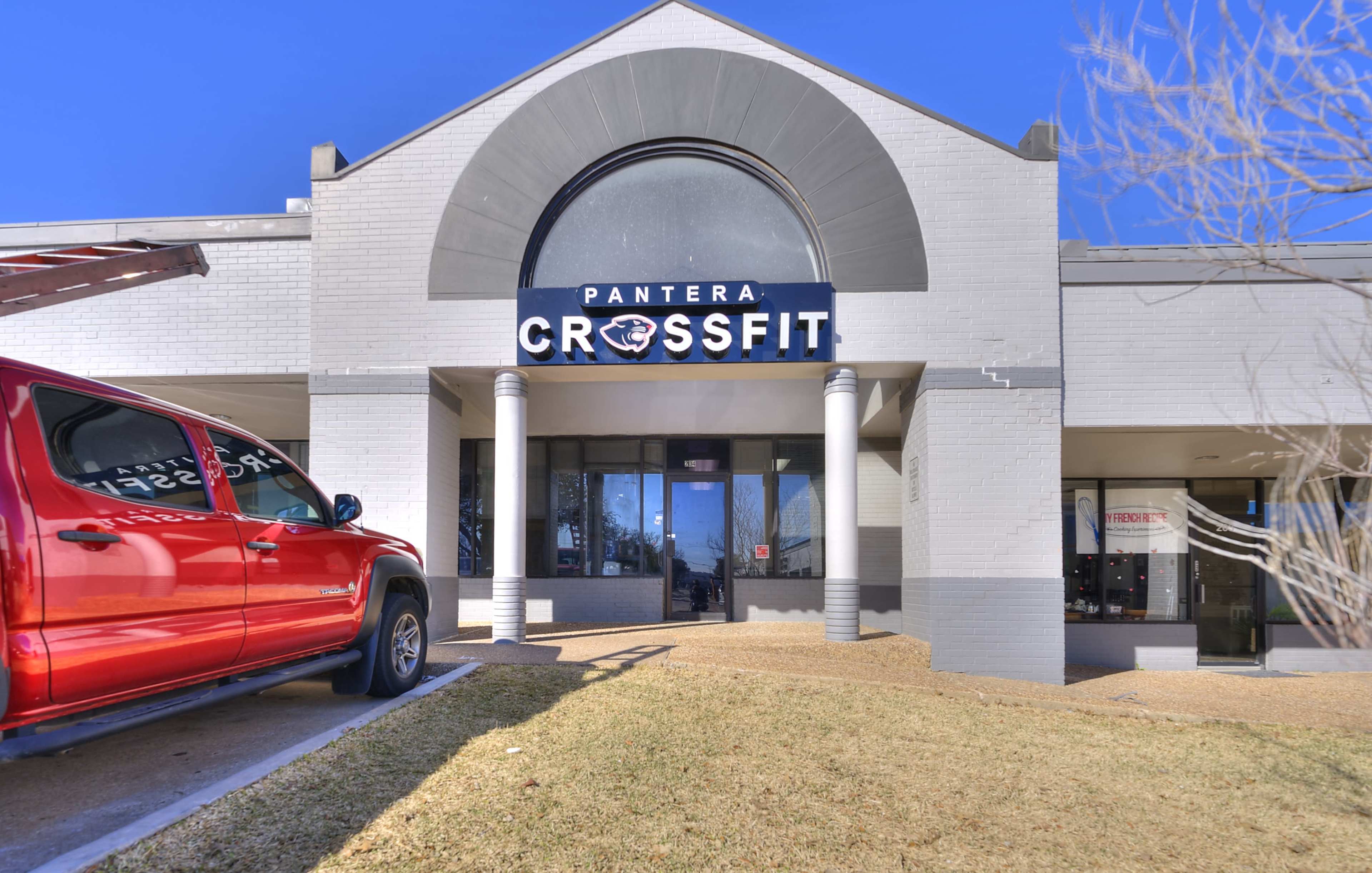 A building facade displaying the sign "Pantera CrossFit," with a red truck parked nearby on a grassy area.