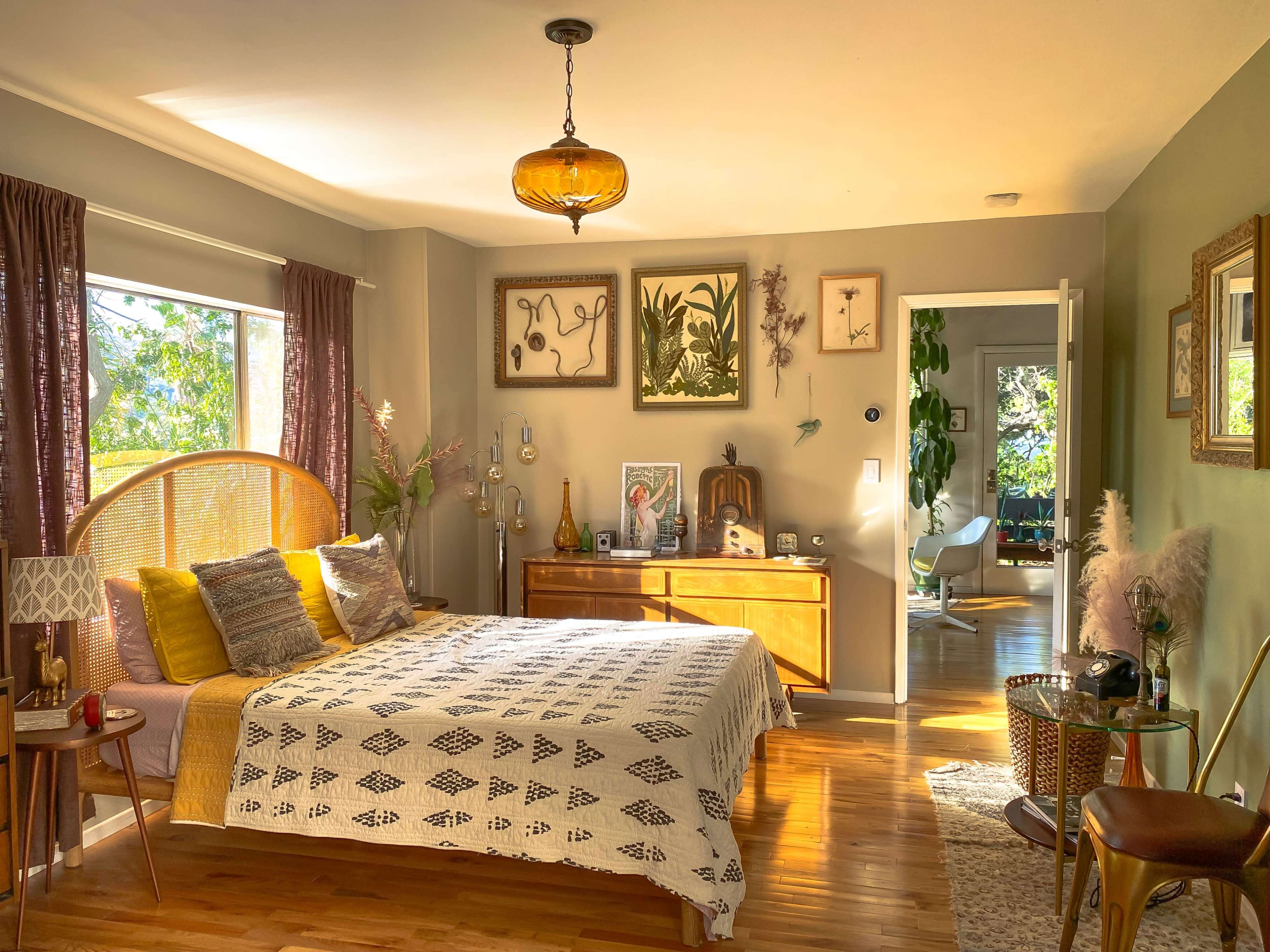 A cozy bedroom with a wooden bed, decorative plants, and natural light streaming through the windows.