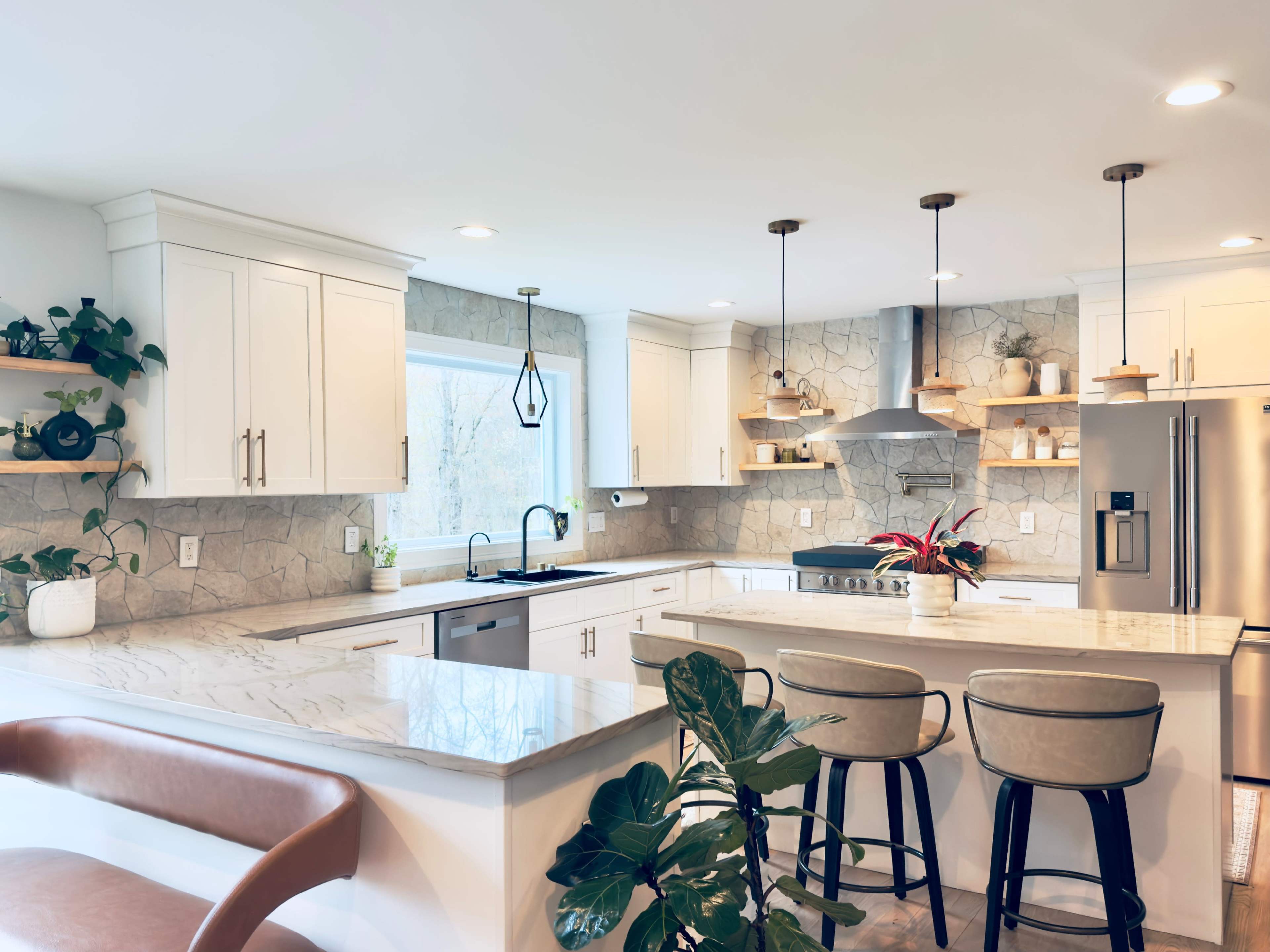 The image shows a modern kitchen featuring white cabinets, a stone backsplash, a large island with seating, and natural light coming through a window.