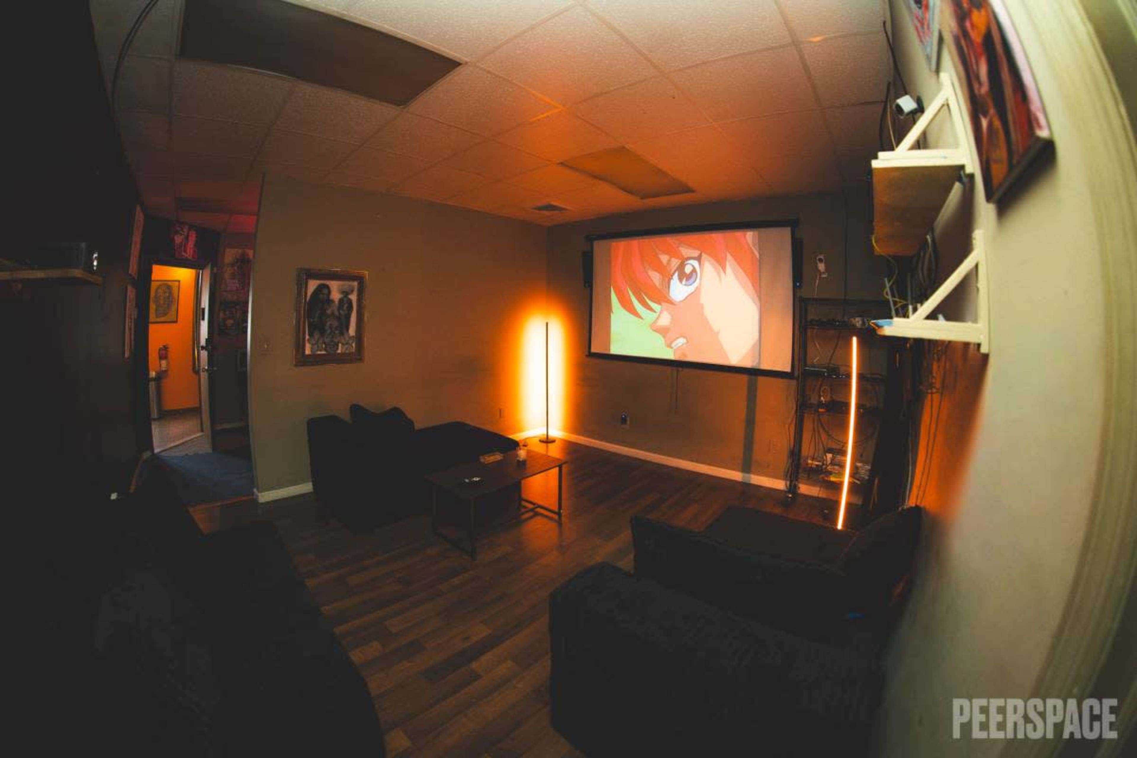 A cozy room features a large projector screen displaying an animated character, with dark couches and a warm light source illuminating the space.