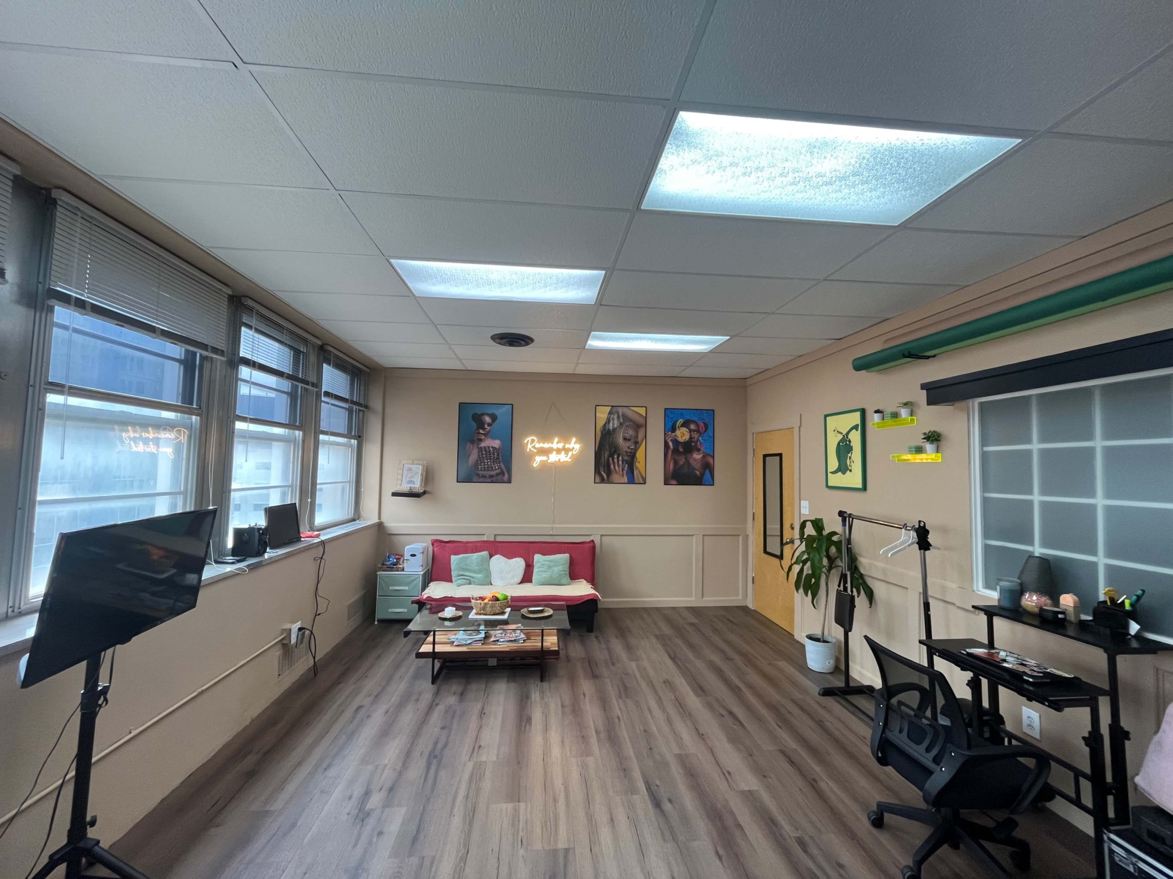 A well-lit office space with a red couch, a coffee table, a desk setup, wall art featuring portraits, and a small plant.