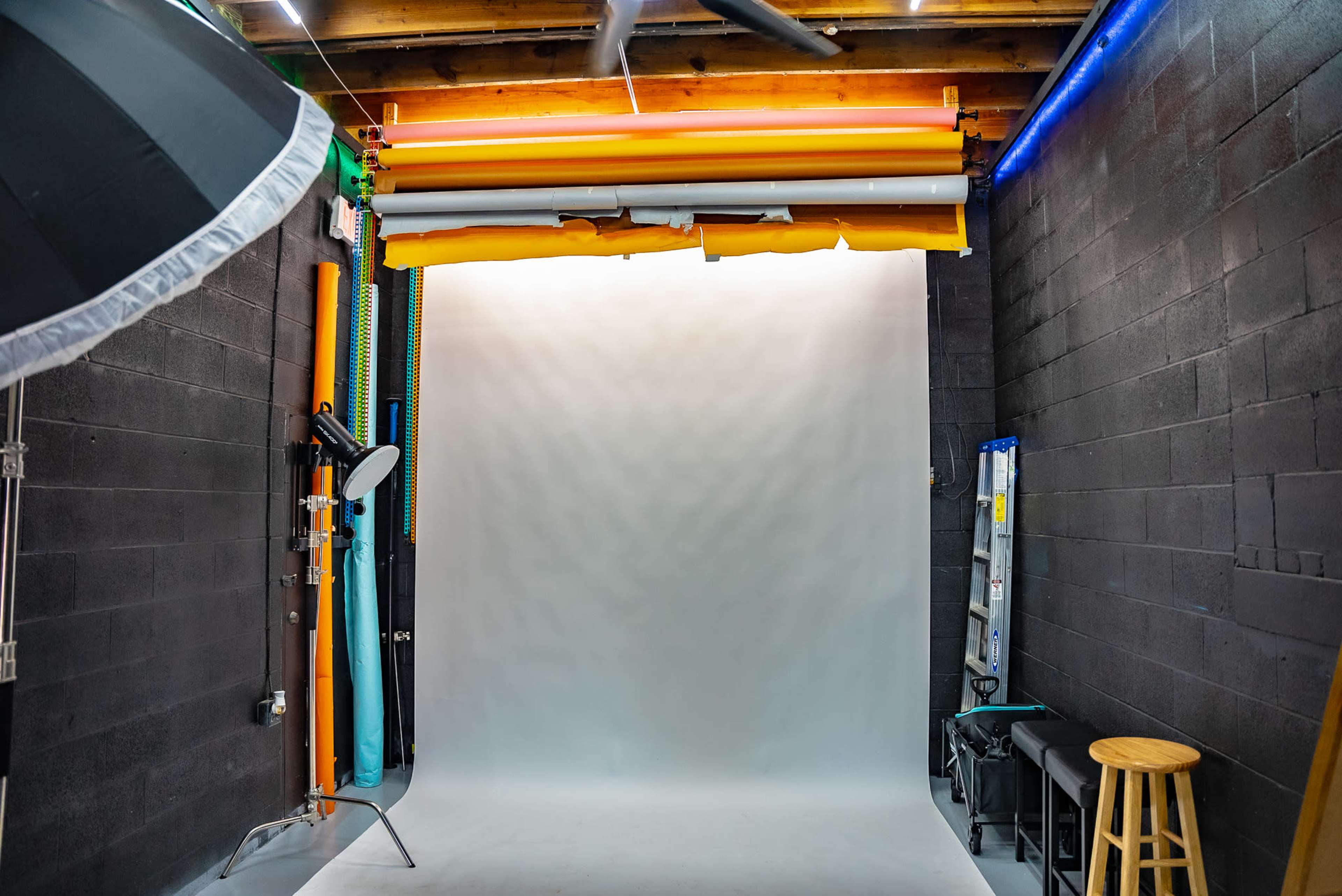 A photography studio with a seamless backdrop, lighting equipment, and various colored rolls of backdrop paper.