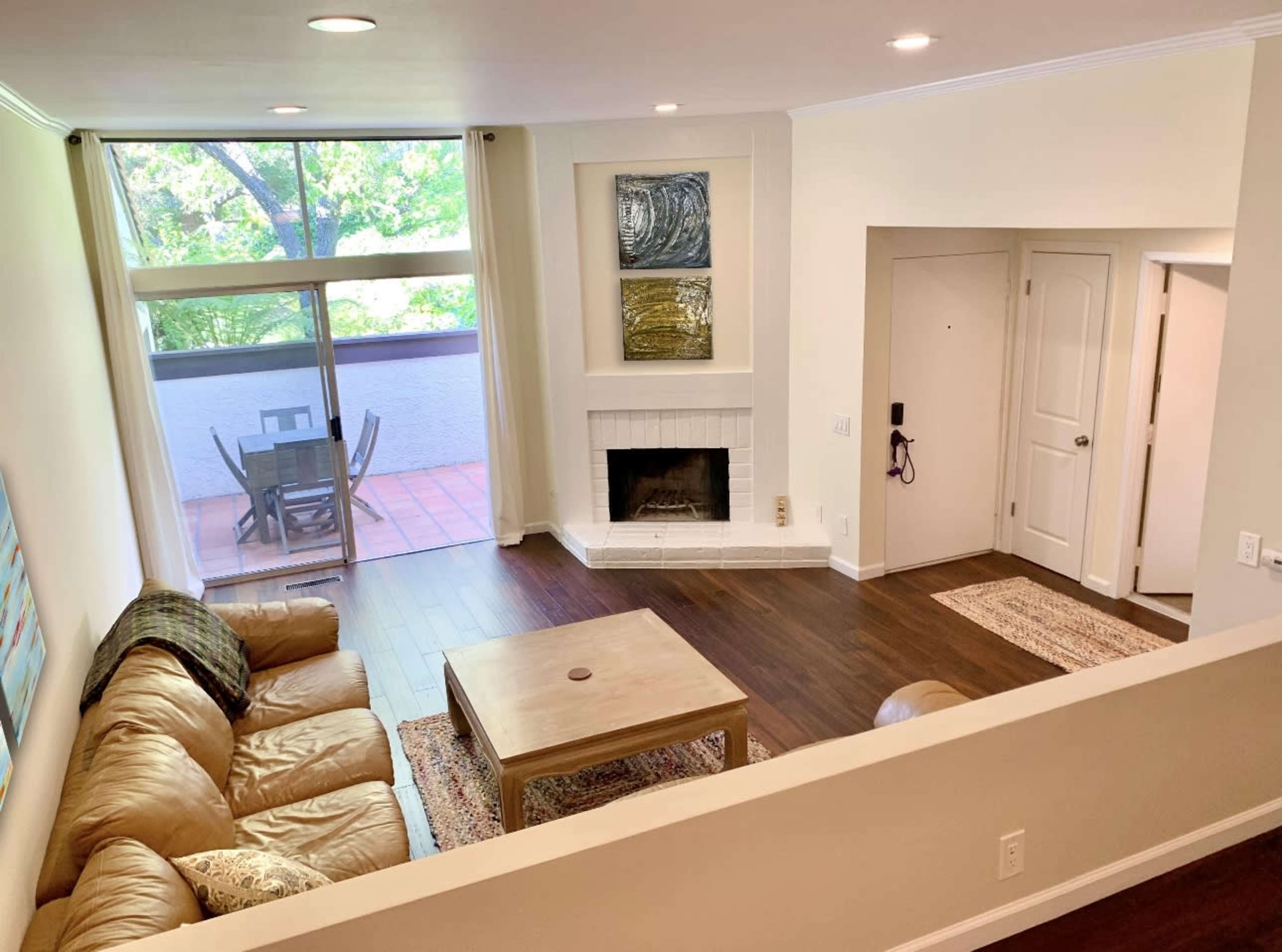 A living room with a tan leather sofa, a wooden coffee table, and a fireplace, adjacent to a dining area with a patio view.