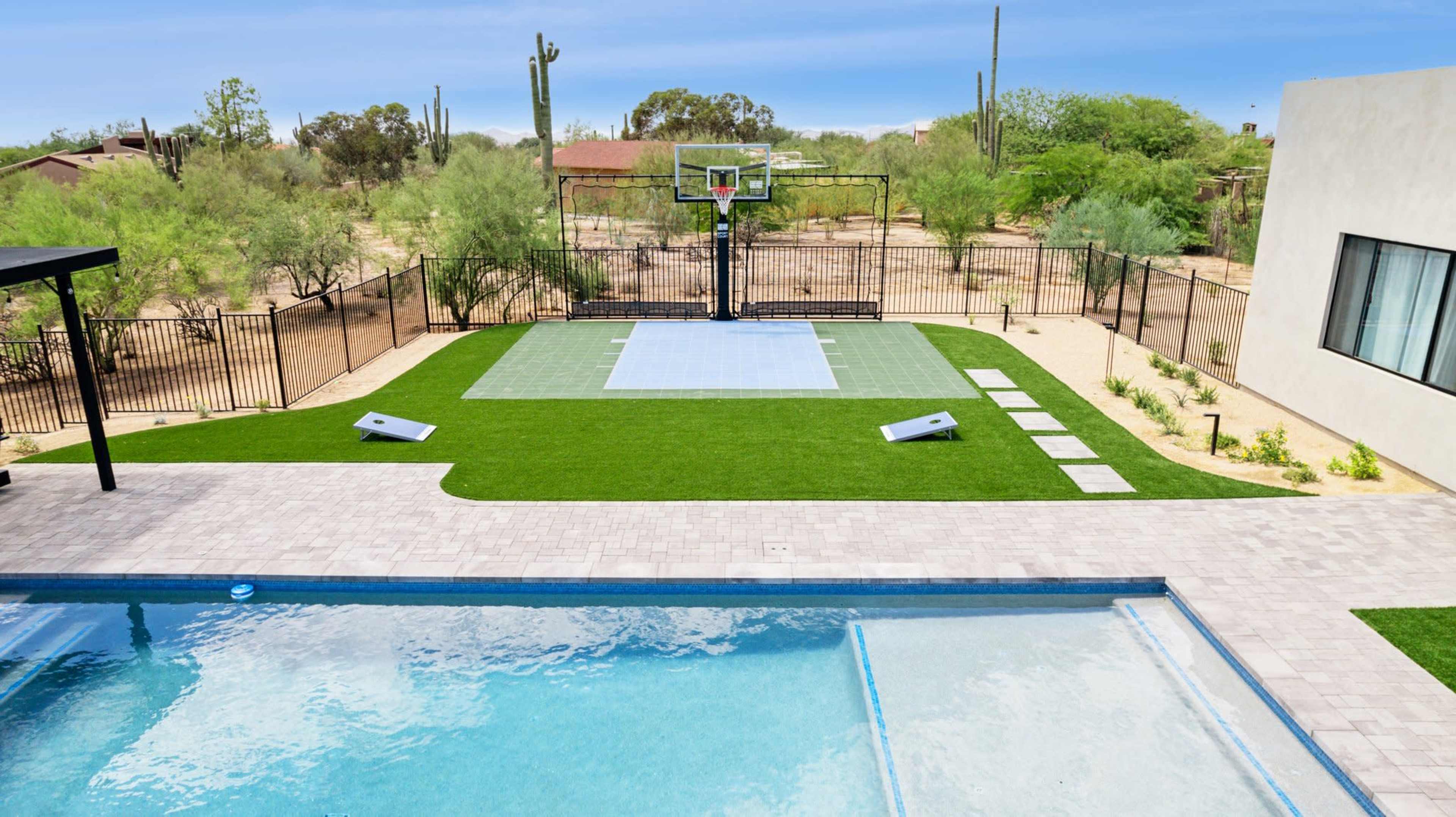 The image shows a backyard featuring a swimming pool, a basketball court with a hoop, and surrounding desert landscaping.
