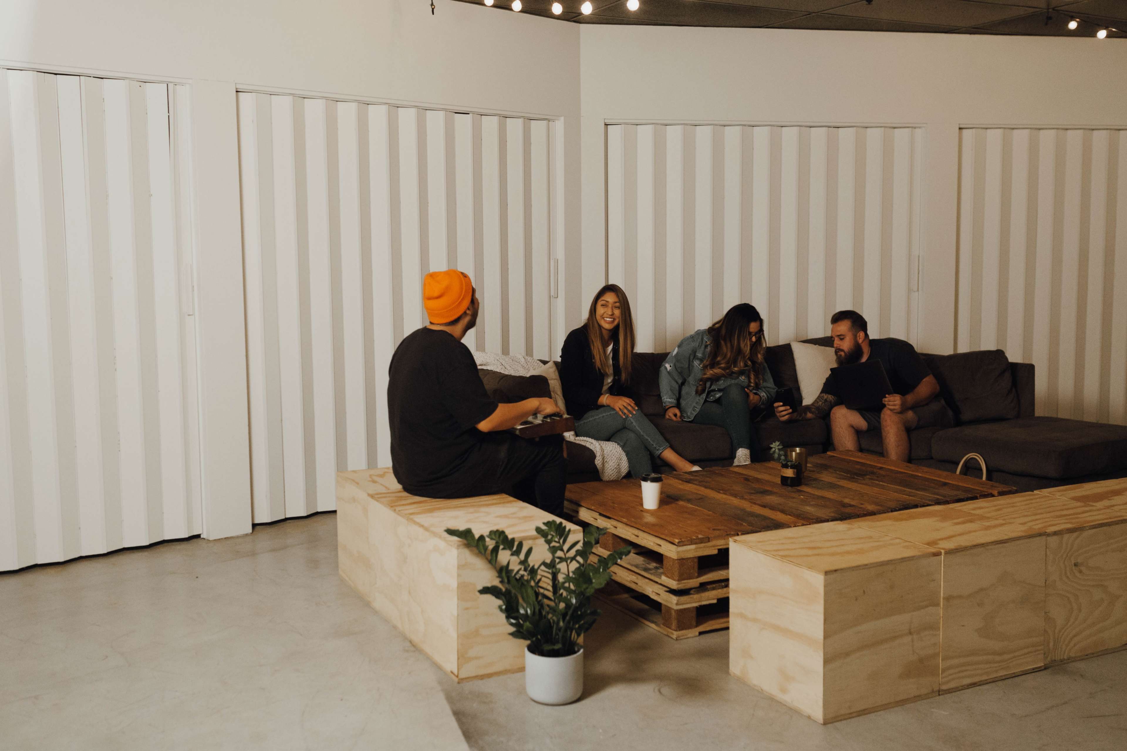 A group of four people sits on a couch and wooden benches in a brightly lit, minimalistic room.