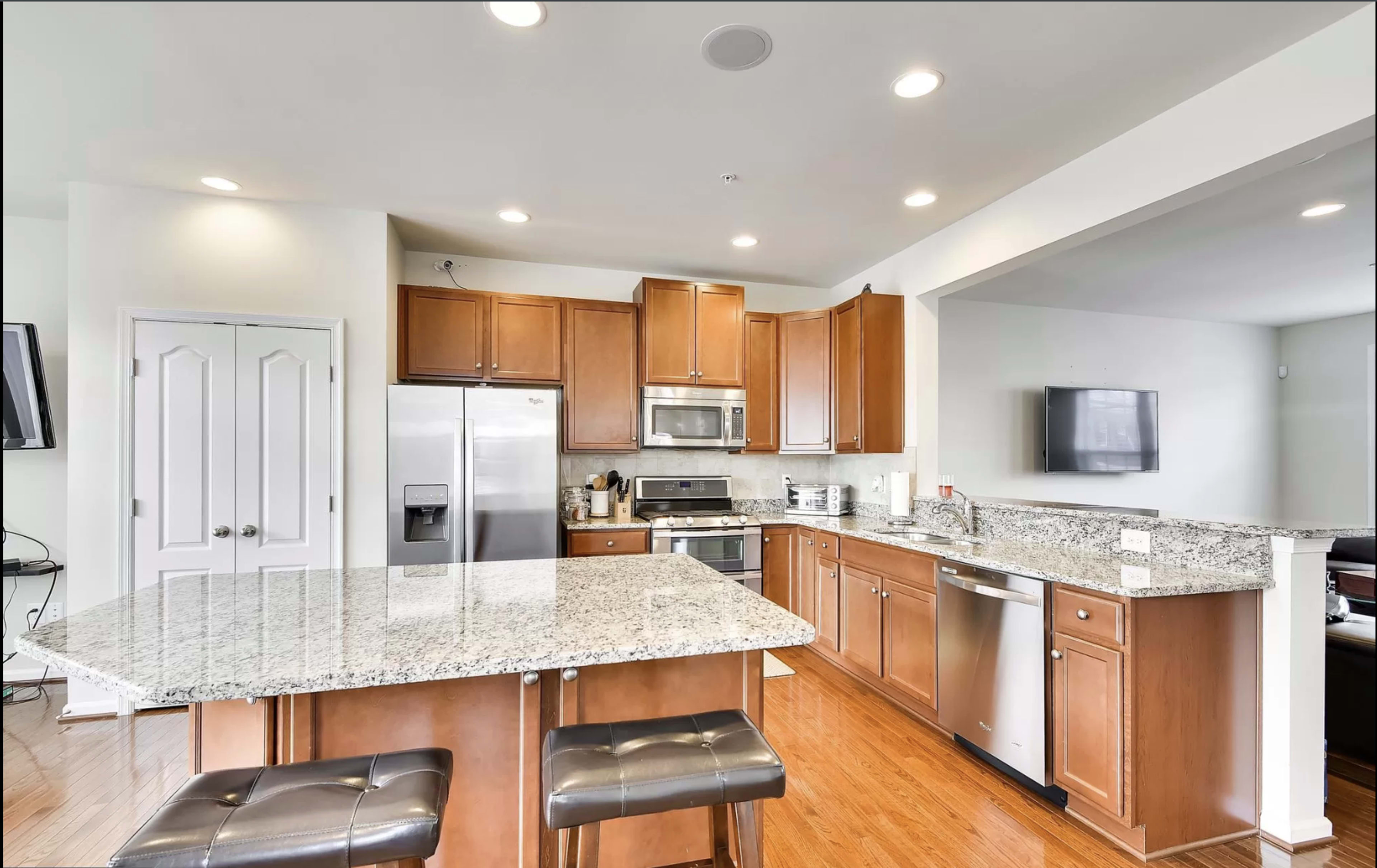 A modern kitchen featuring wooden cabinets, a granite countertop island, stainless steel appliances, and hardwood flooring.