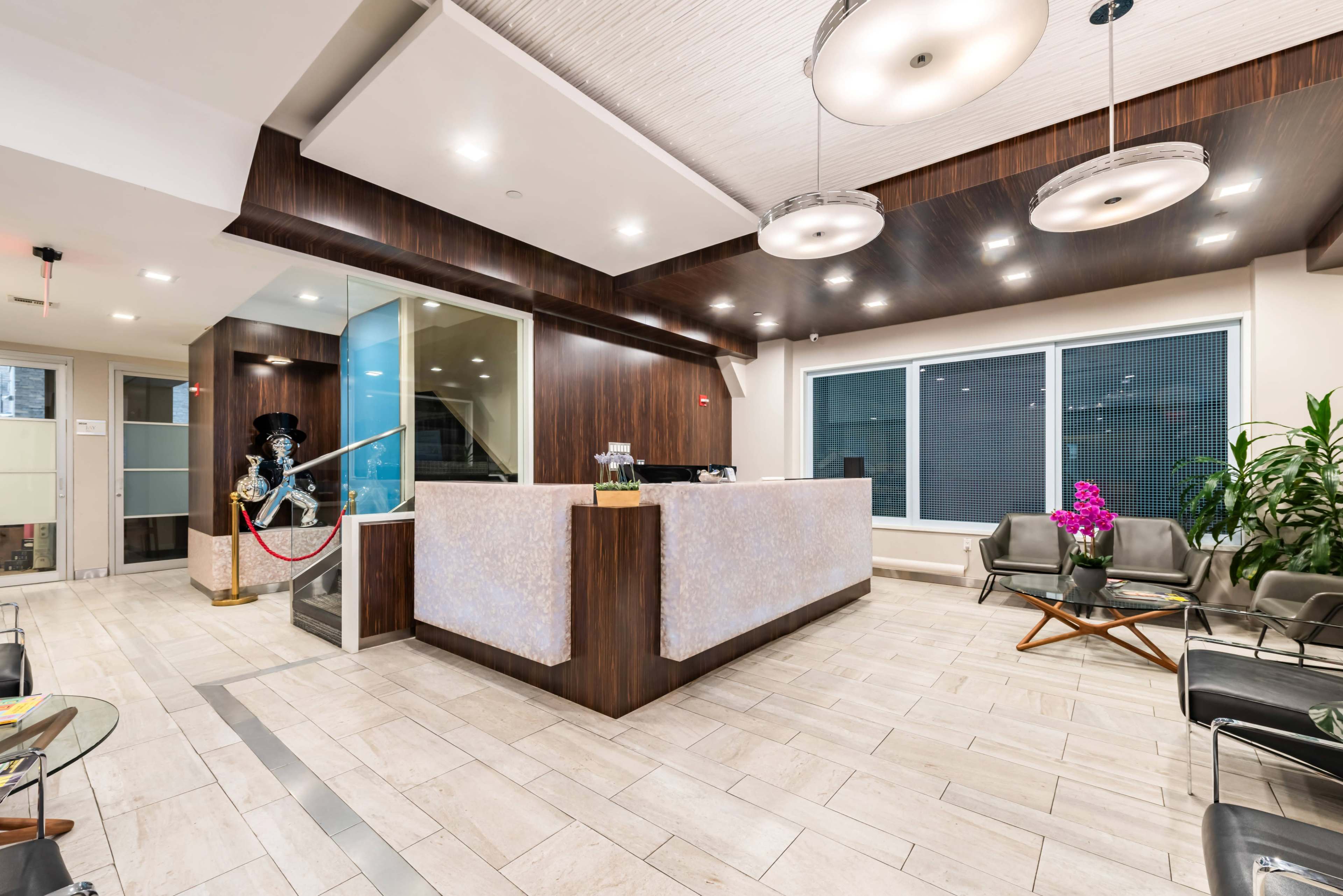 The image shows a modern reception area with a glossy front desk, comfortable seating, large windows, and decorative plants.