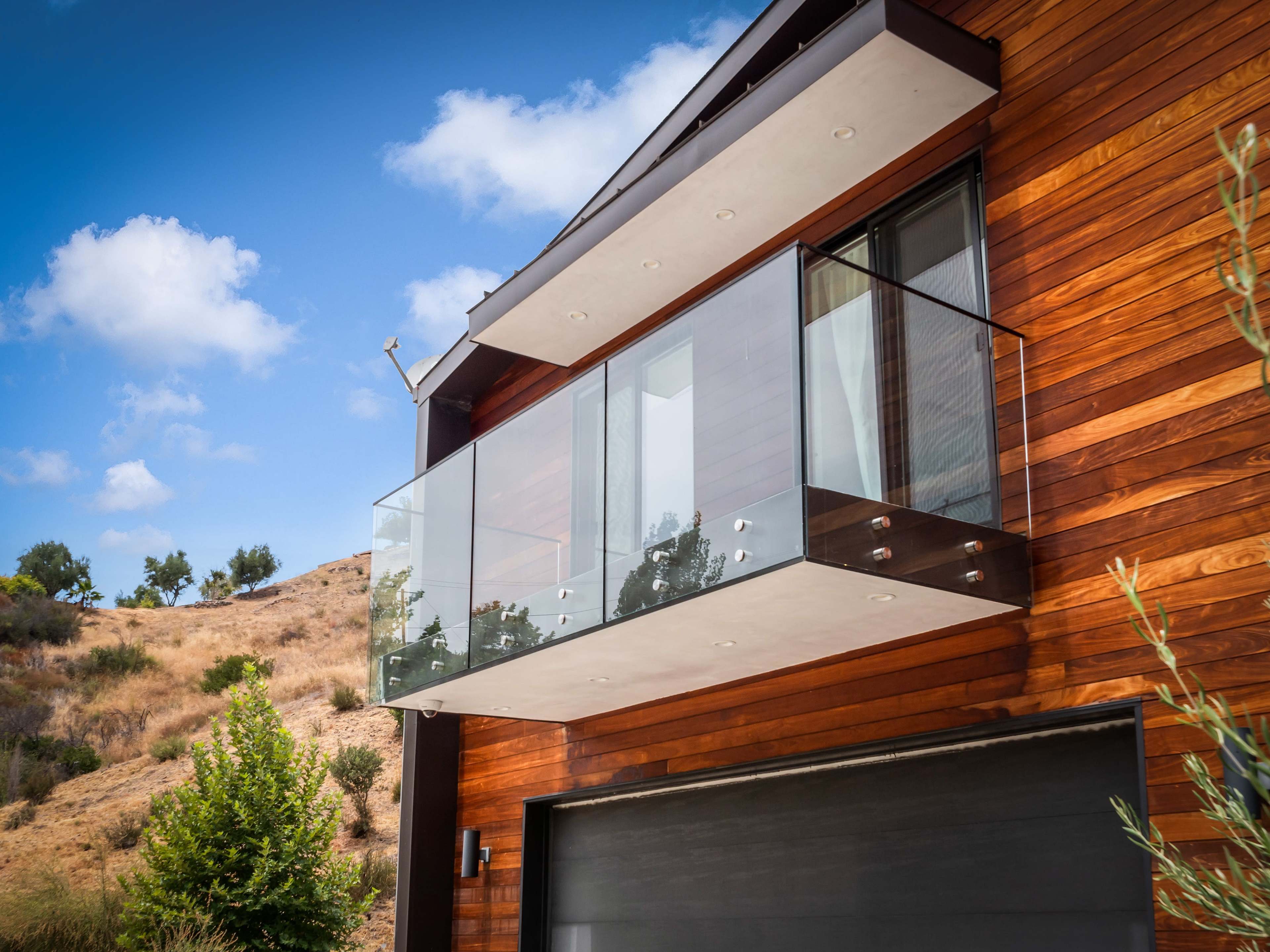 A modern house with a wooden exterior and a glass balcony overlooking a hillside.