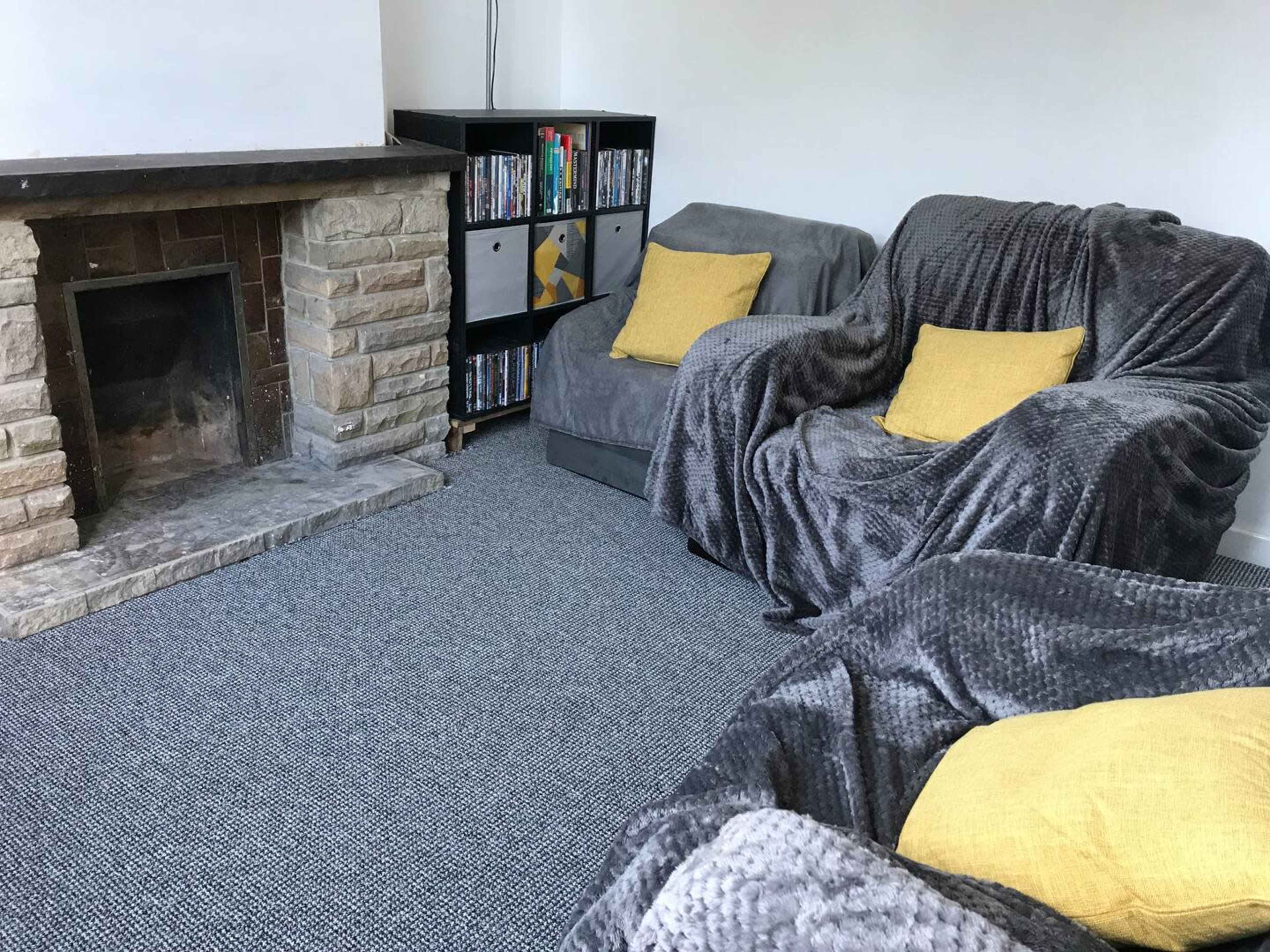 A living room with two gray sofas, a stone fireplace, and a bookshelf filled with DVDs.