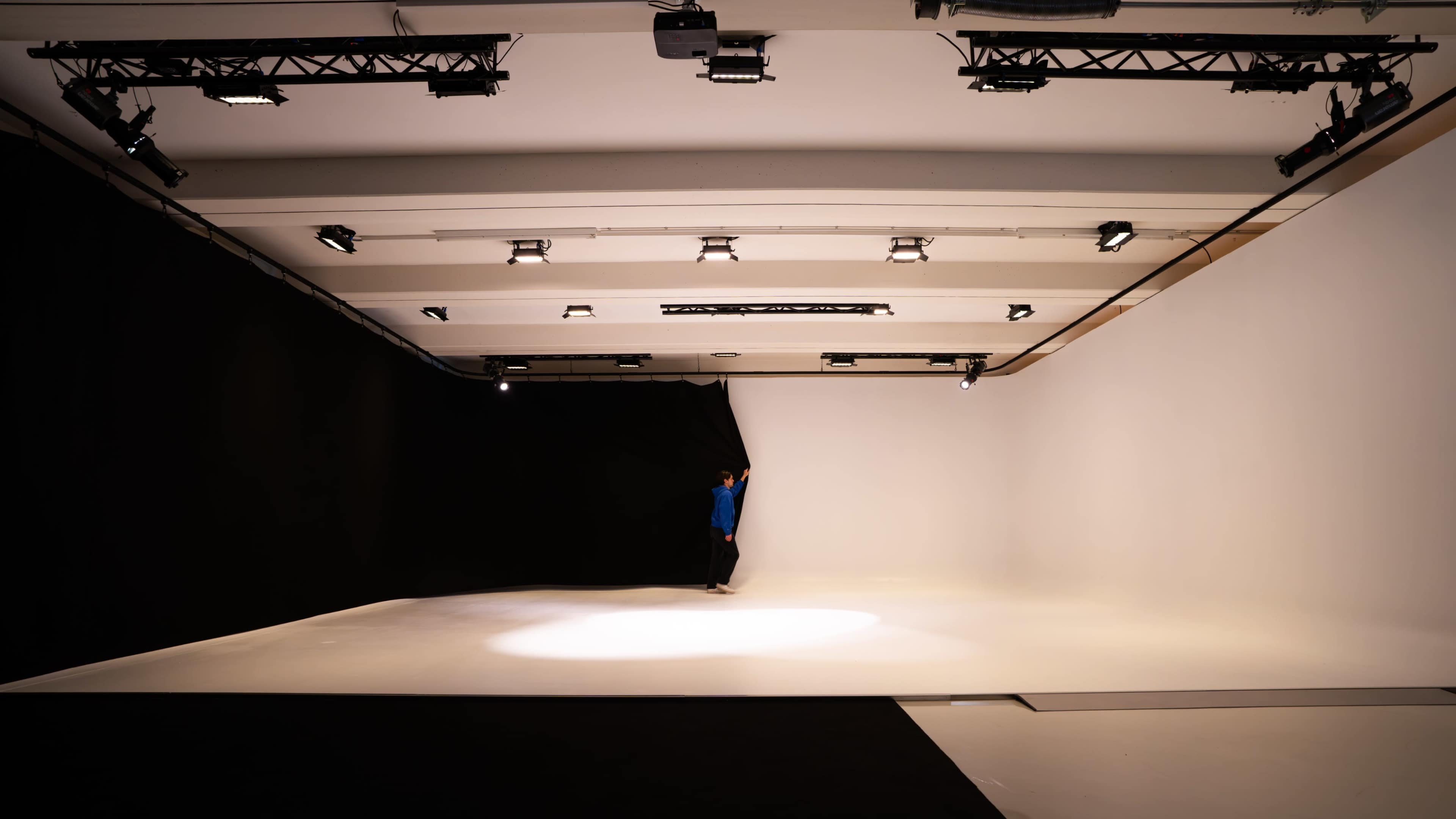 A person pulls back a black curtain in a spacious photography studio with white and black backdrops.