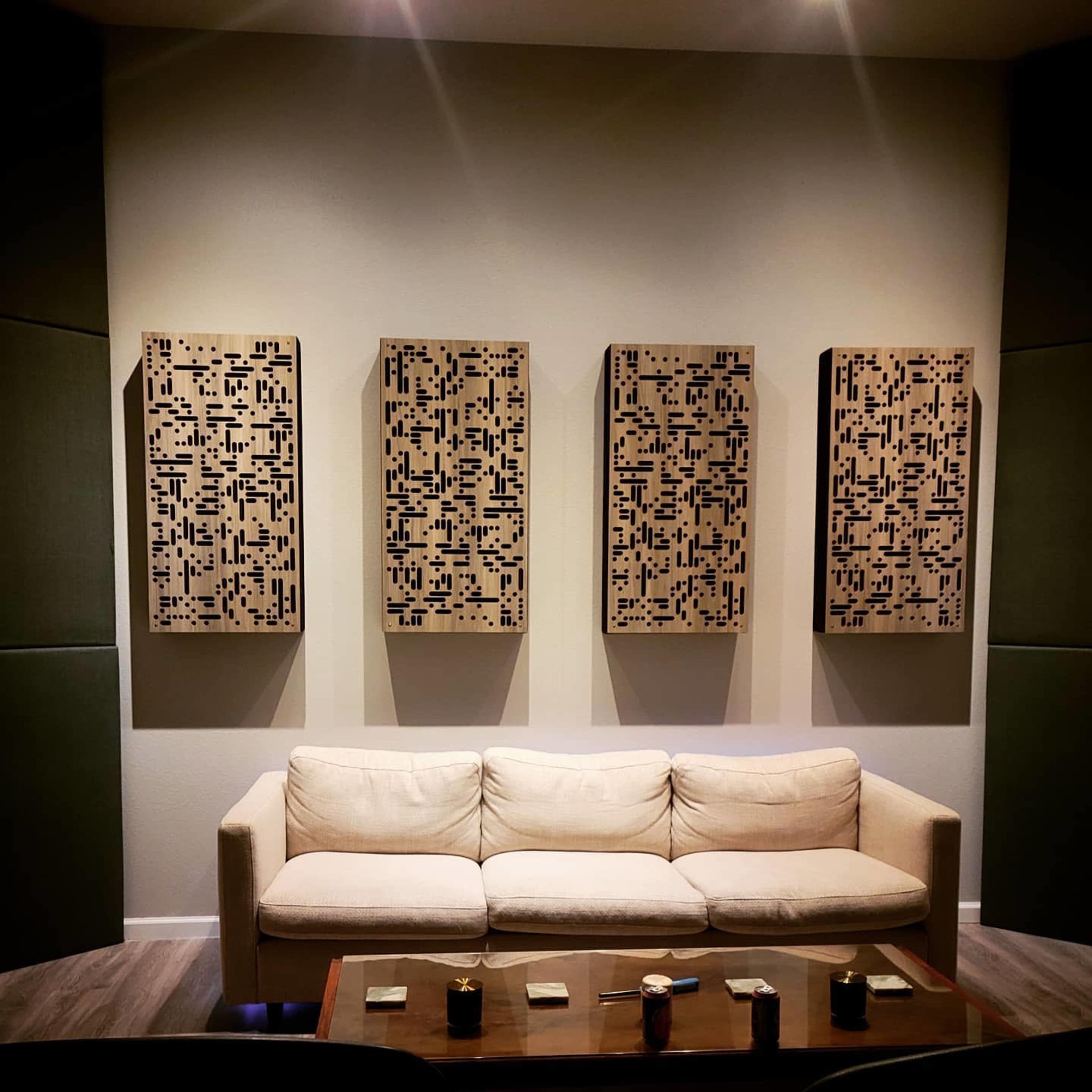 A light-colored sofa placed against a wall featuring four rectangular art panels with a geometric design, illuminated by overhead lighting.