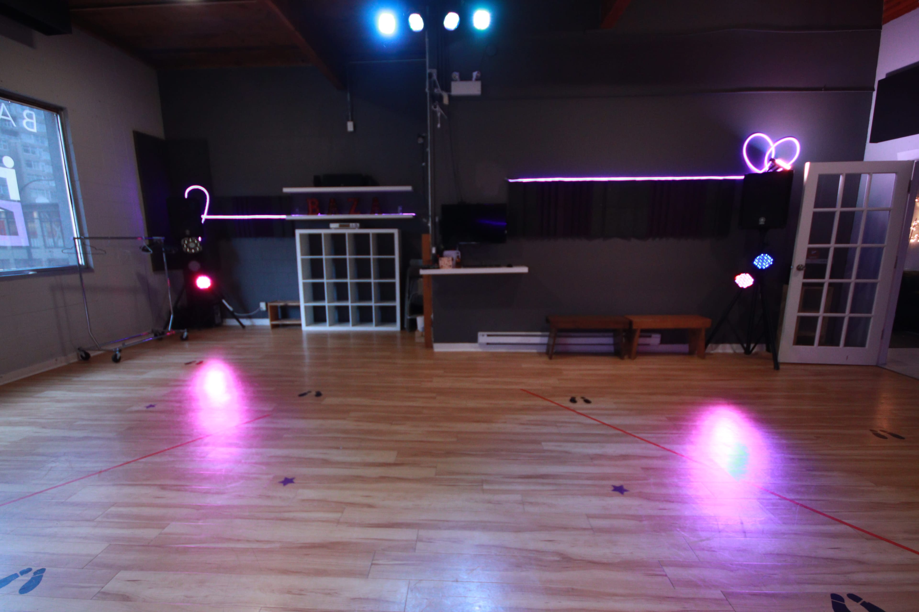 An empty dance studio with wooden floors, colored stage lights, and a mirrored wall.