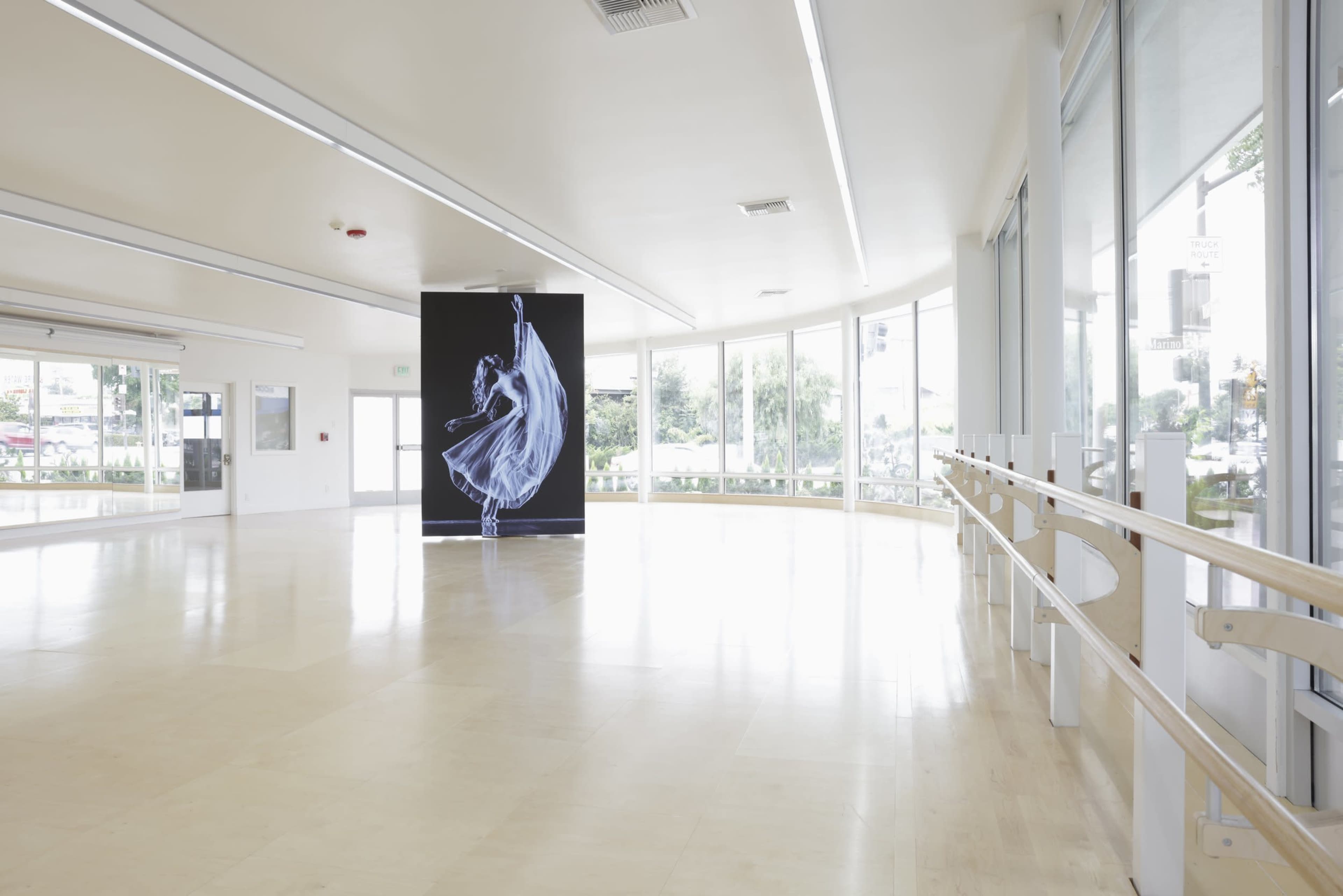 The image shows a spacious dance studio with large windows and a digital display of a dancer in motion against a black background.