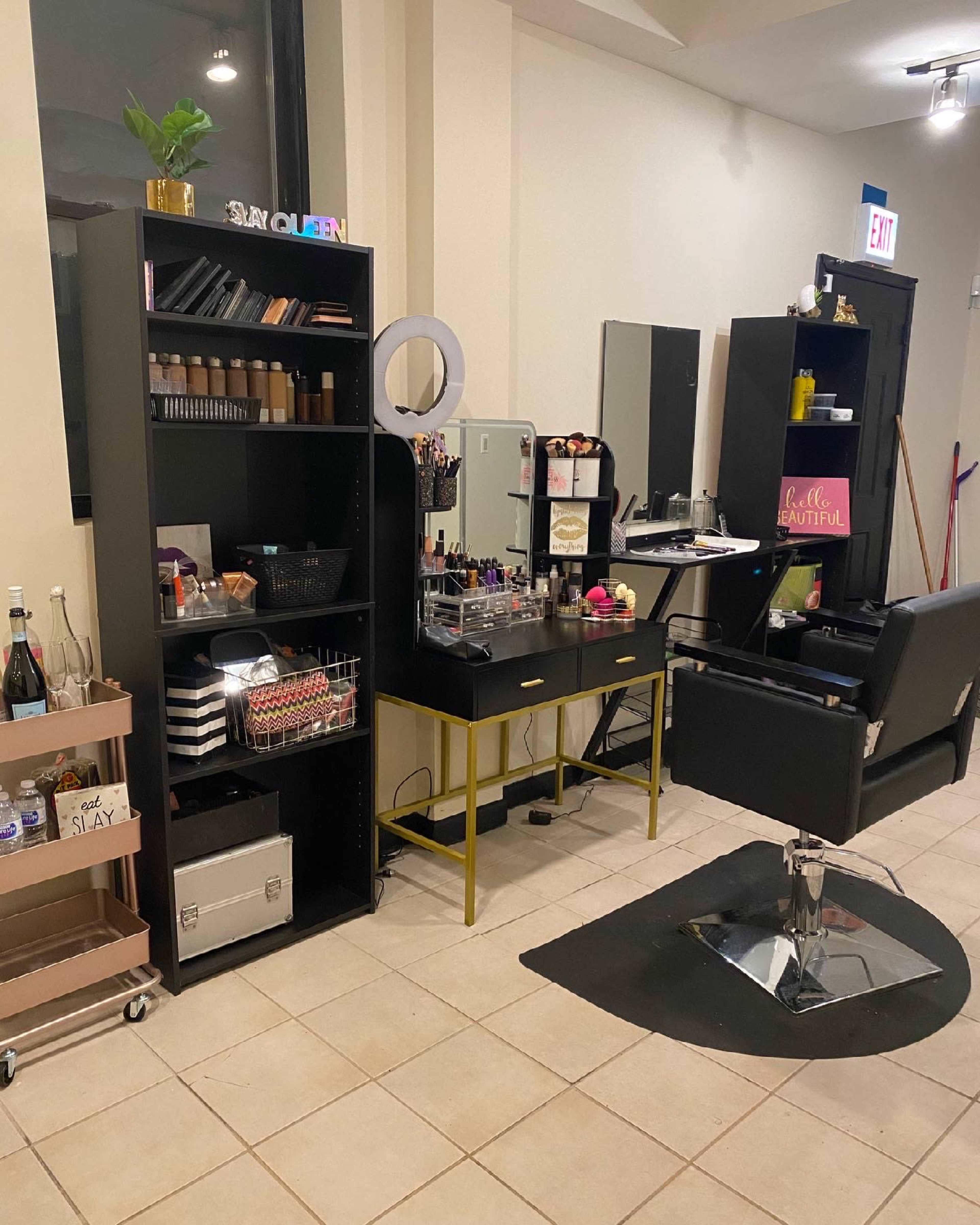 A makeup station with black shelving units, a mirror, and a chair, all set up in a well-lit room.