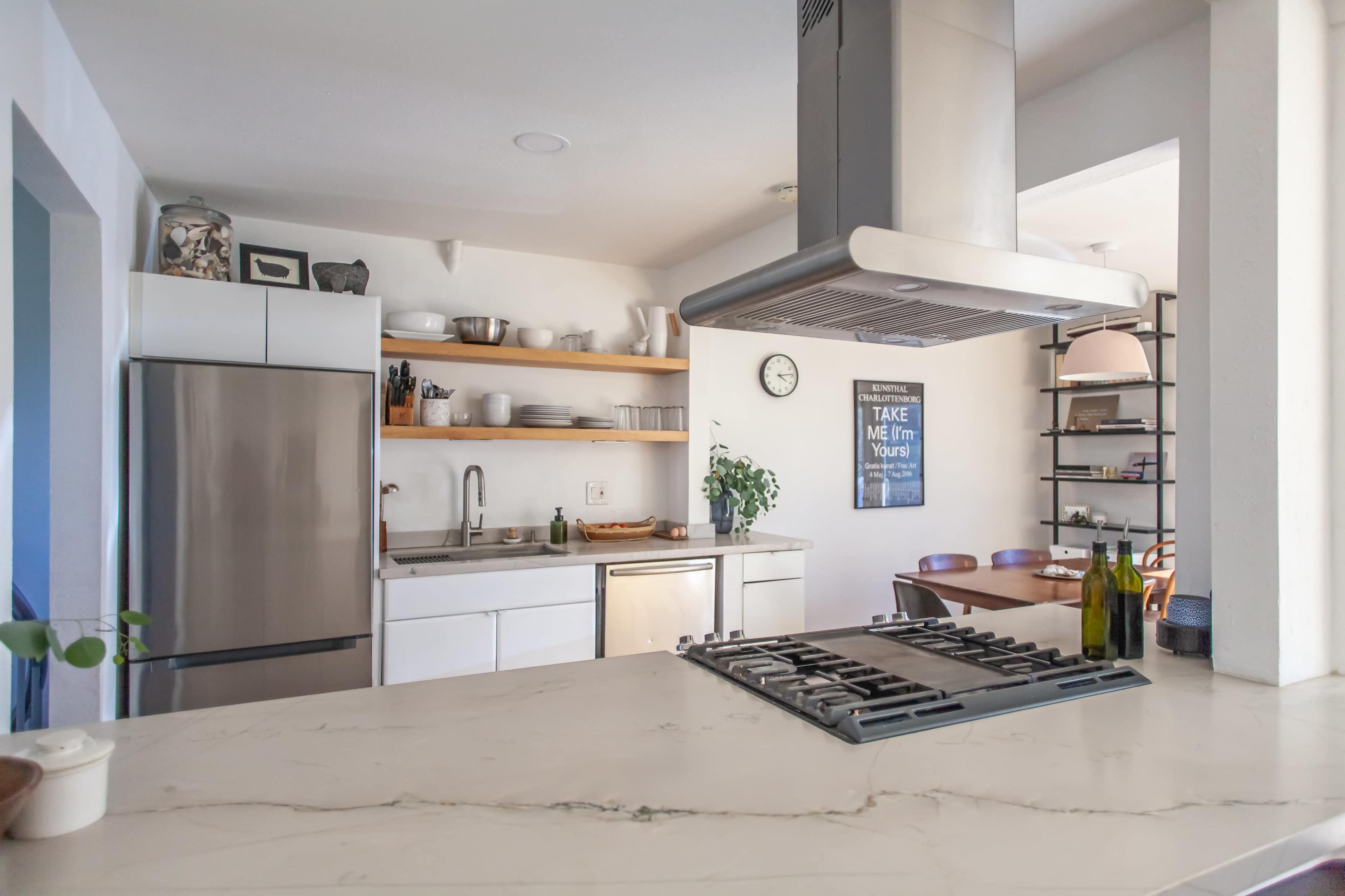 A modern kitchen features stainless steel appliances, open shelving, and a gas stove with a large hood.