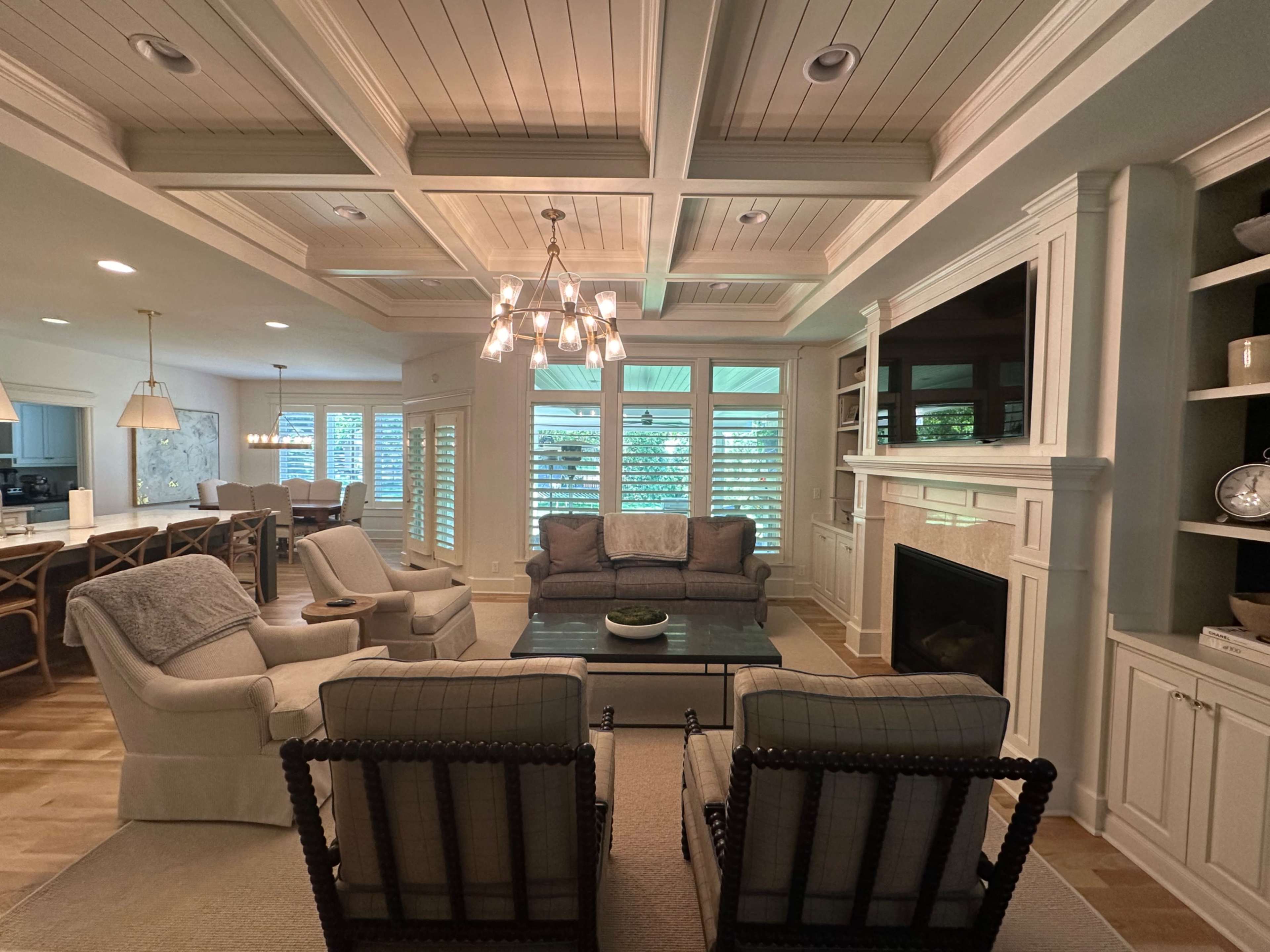 A spacious living room features a coffered ceiling, a cozy seating arrangement with a couch and chairs, and a fireplace surrounded by built-in shelves.