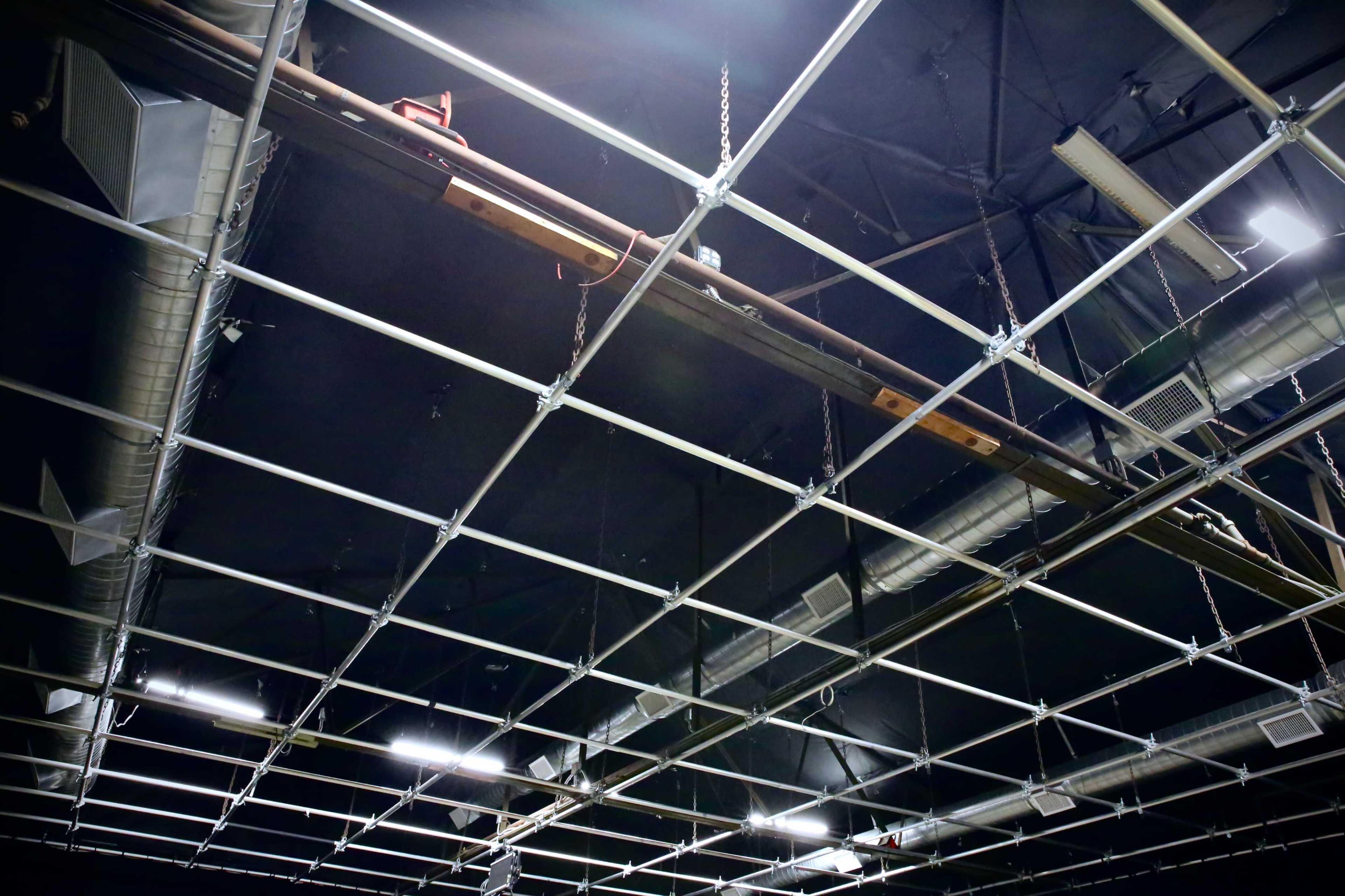 A ceiling framework with exposed pipes and lighting fixtures suspended in a grid arrangement.