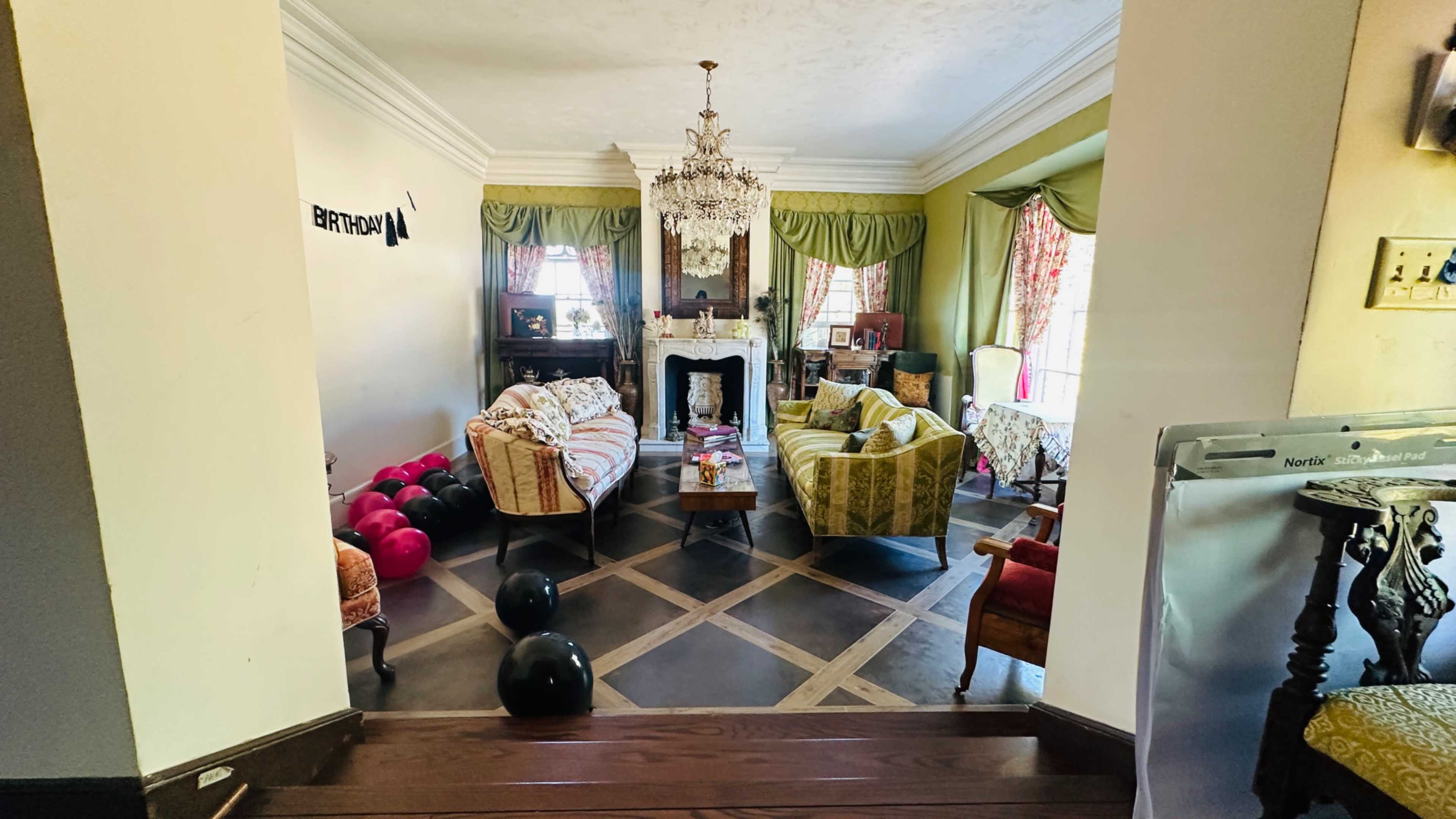 A living room is decorated with colorful furniture and a chandelier, featuring a fireplace and various balloons scattered on the floor.