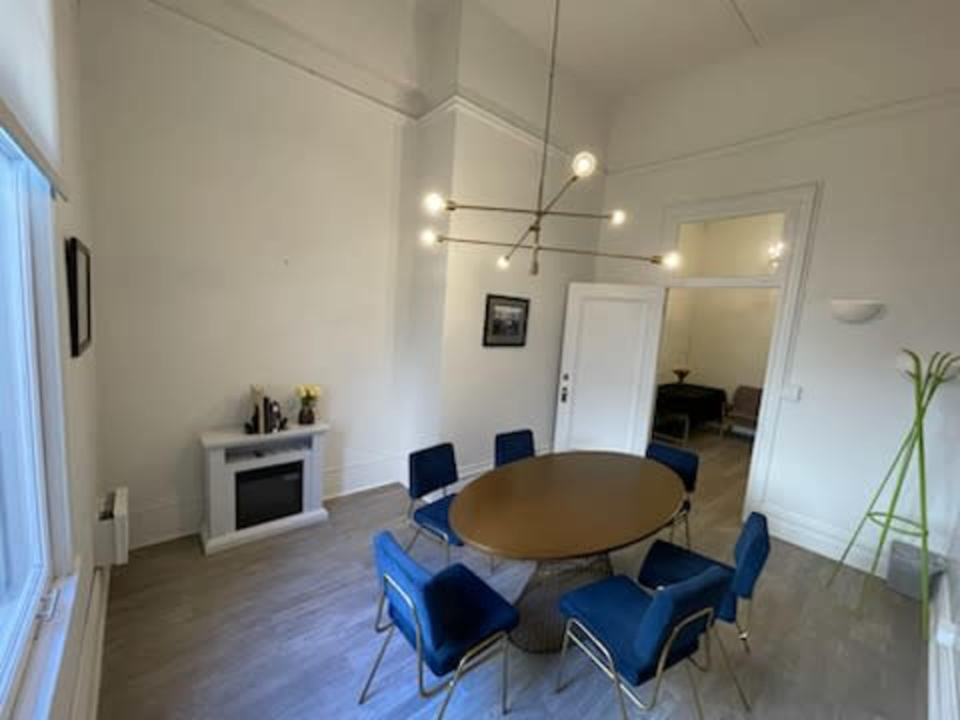 A spacious room features a round table with six blue chairs, a modern light fixture, and a small white fireplace.