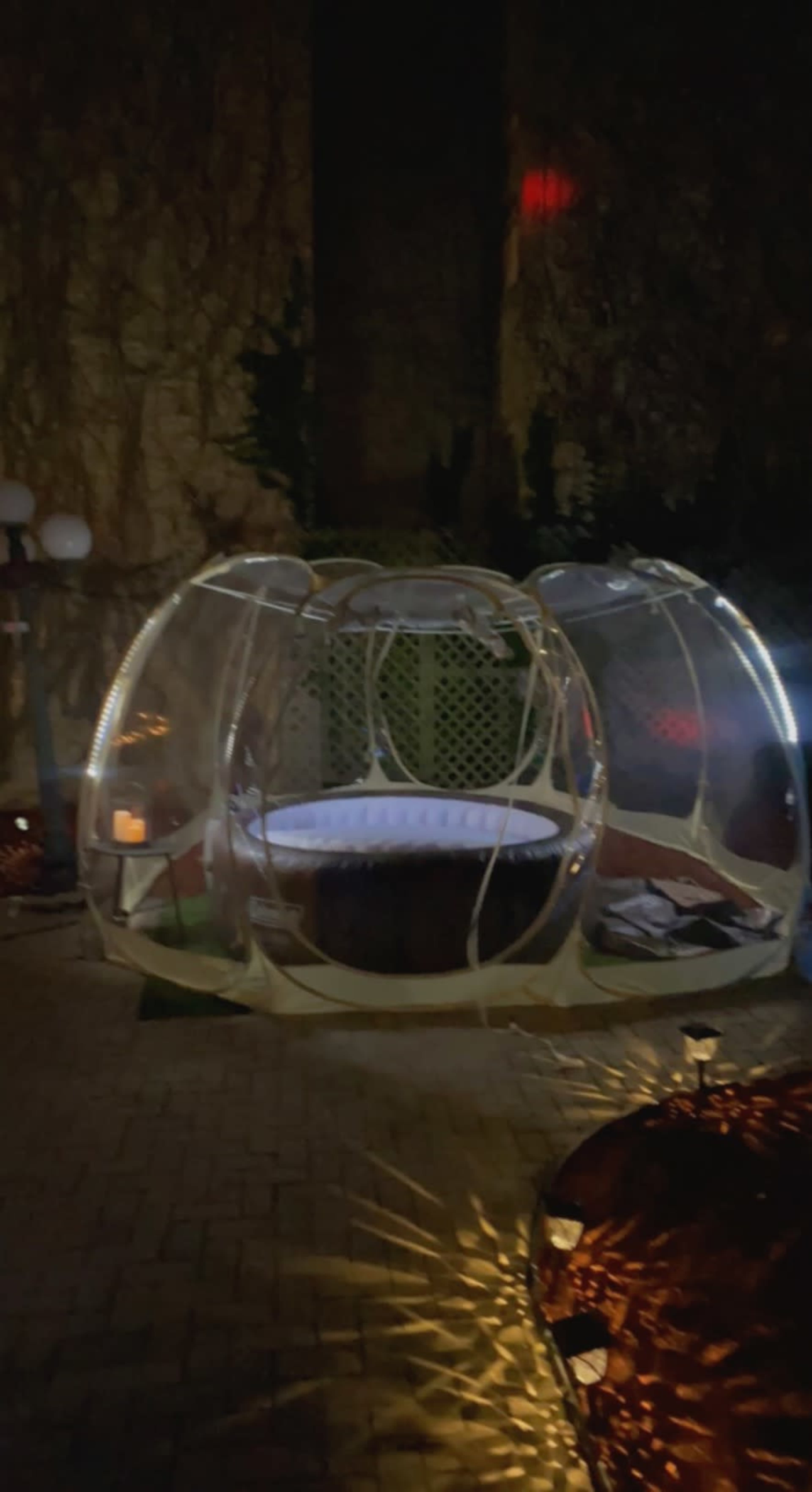 A illuminated transparent enclosure sits in a dark garden, surrounded by soft lighting and landscaping.
